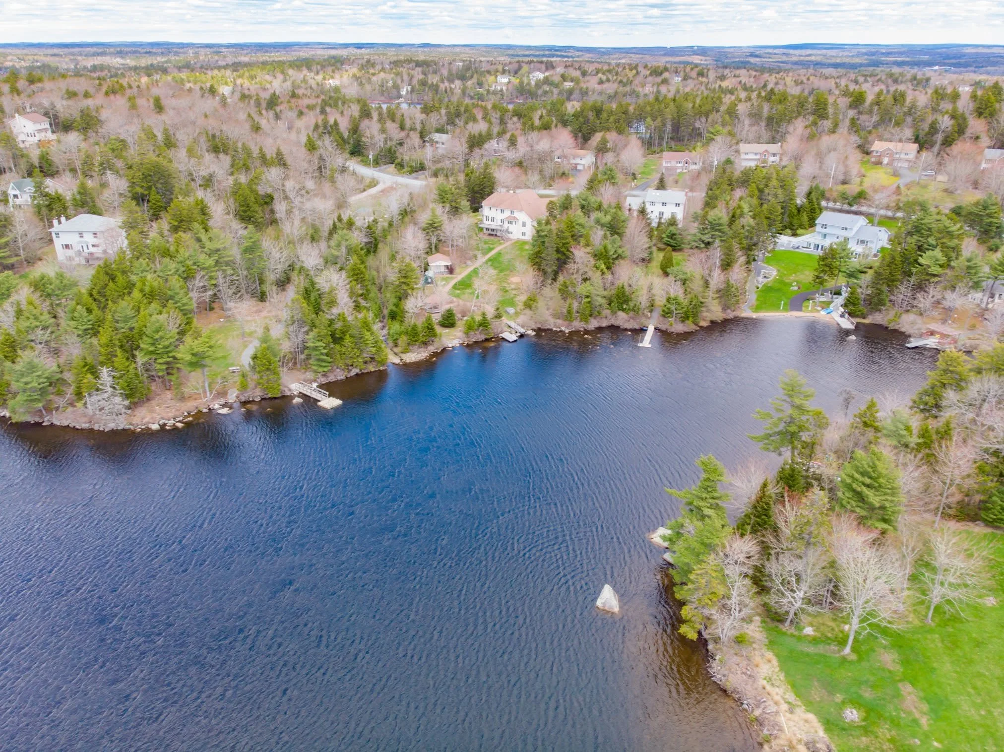 Aerial view of waterfront homes tucked into dense forest along a lake shore in Hammonds Plains.