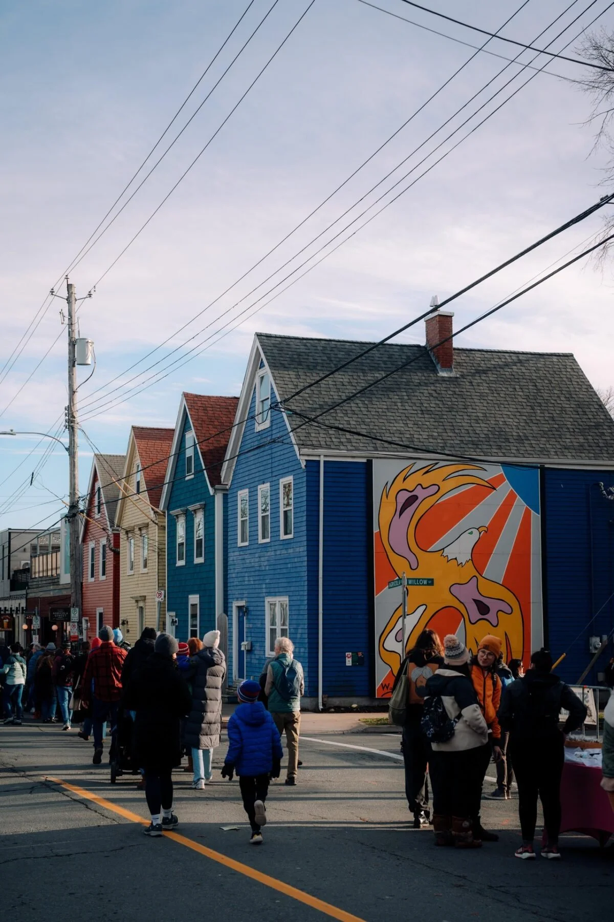 Pedestrians walking past colorful character homes and a street mural on Agricola Street in North End Halifax, Nova Scotia.
