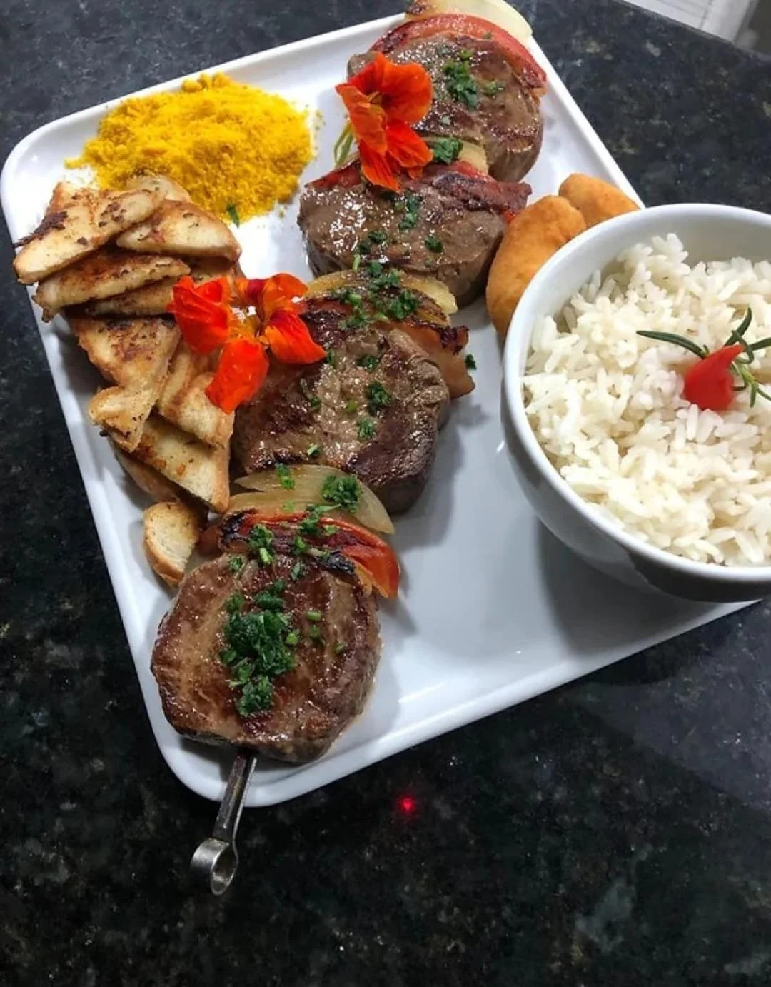 Prato de comida com carne, arroz branco, pão, frutas, queijo, e acompanhamento.