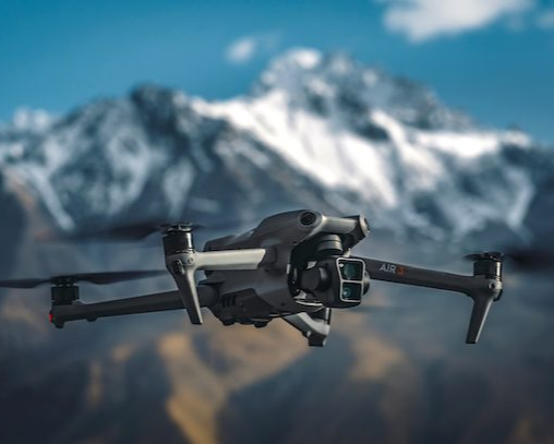 A drone flying in front of snow-capped mountains with a clear blue sky.