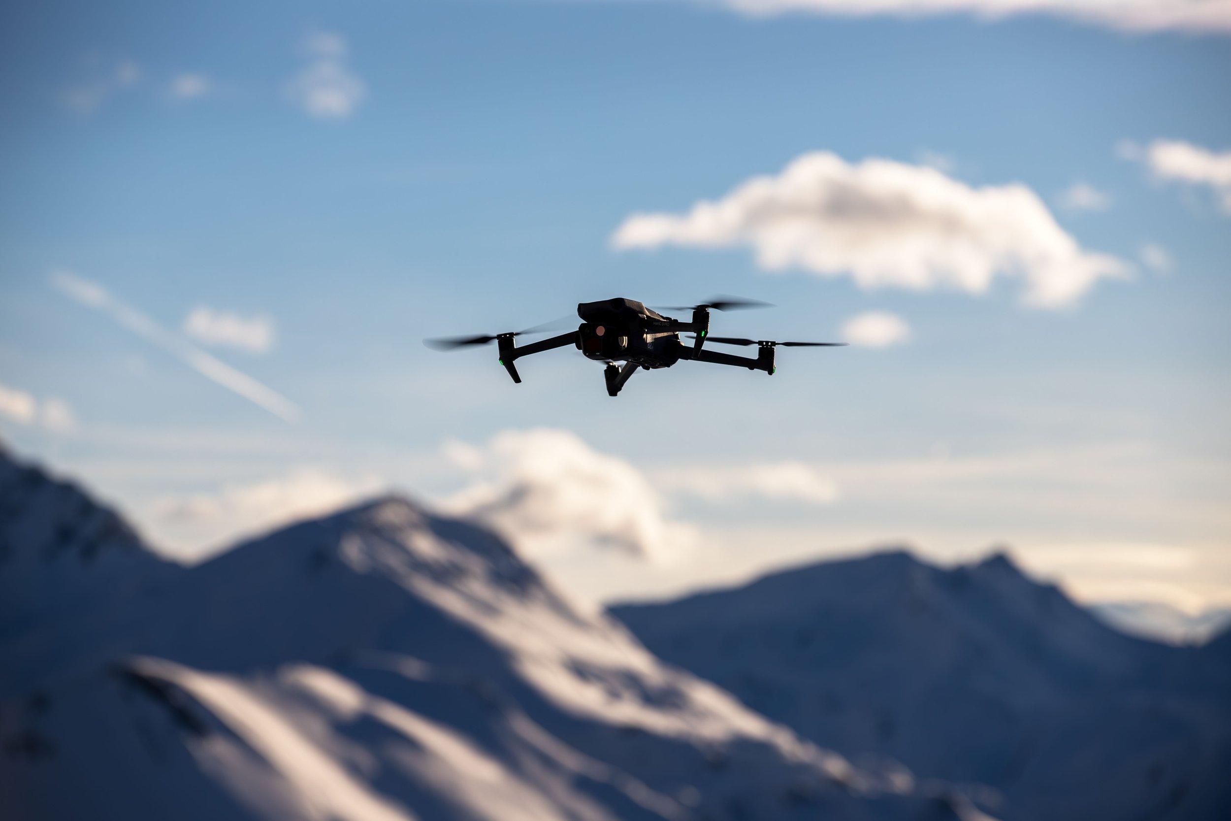 A drone flying in the sky above snowy mountains and clouds.