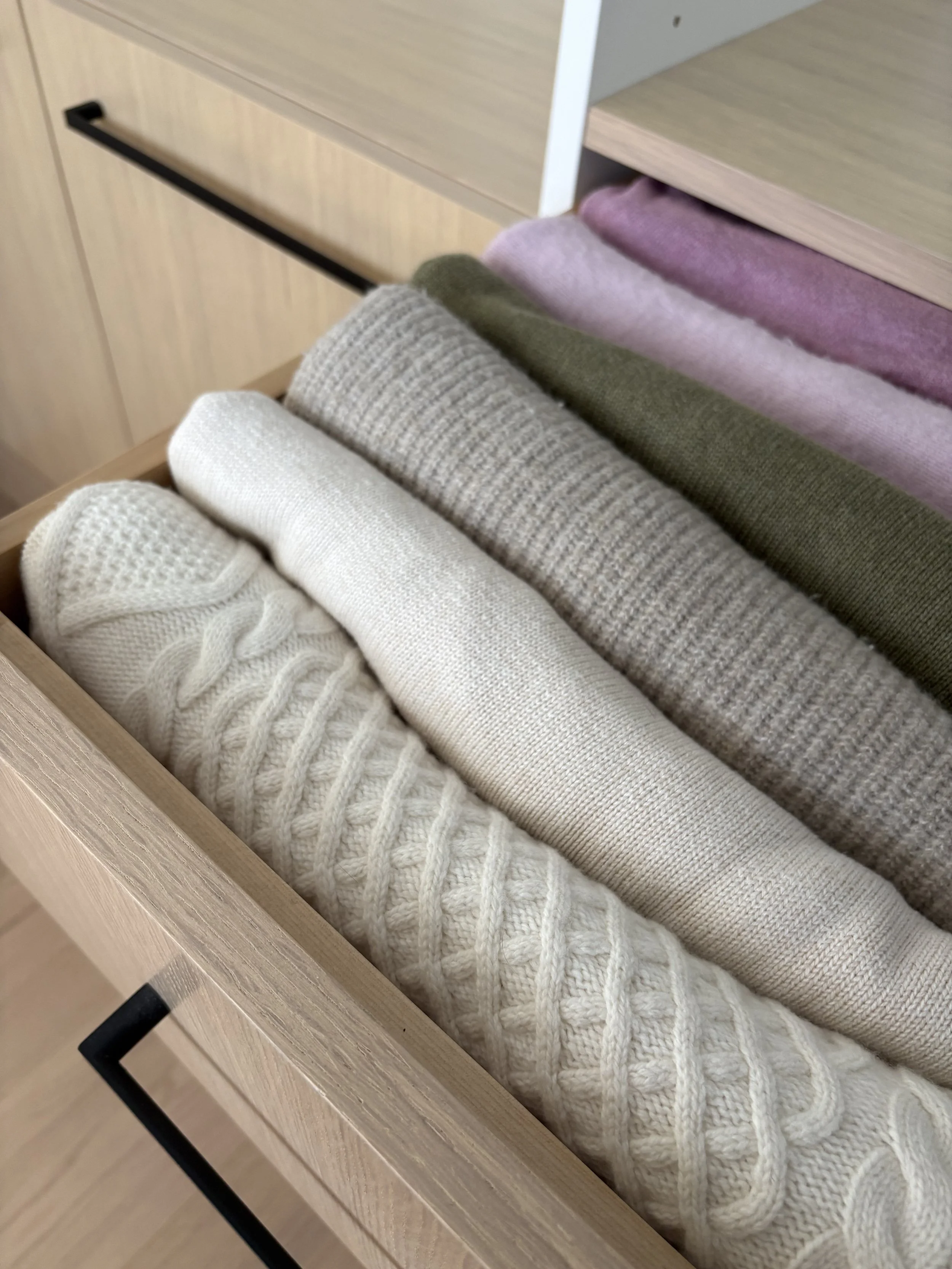 Colourful folded sweaters arranged in a wooden drawer.