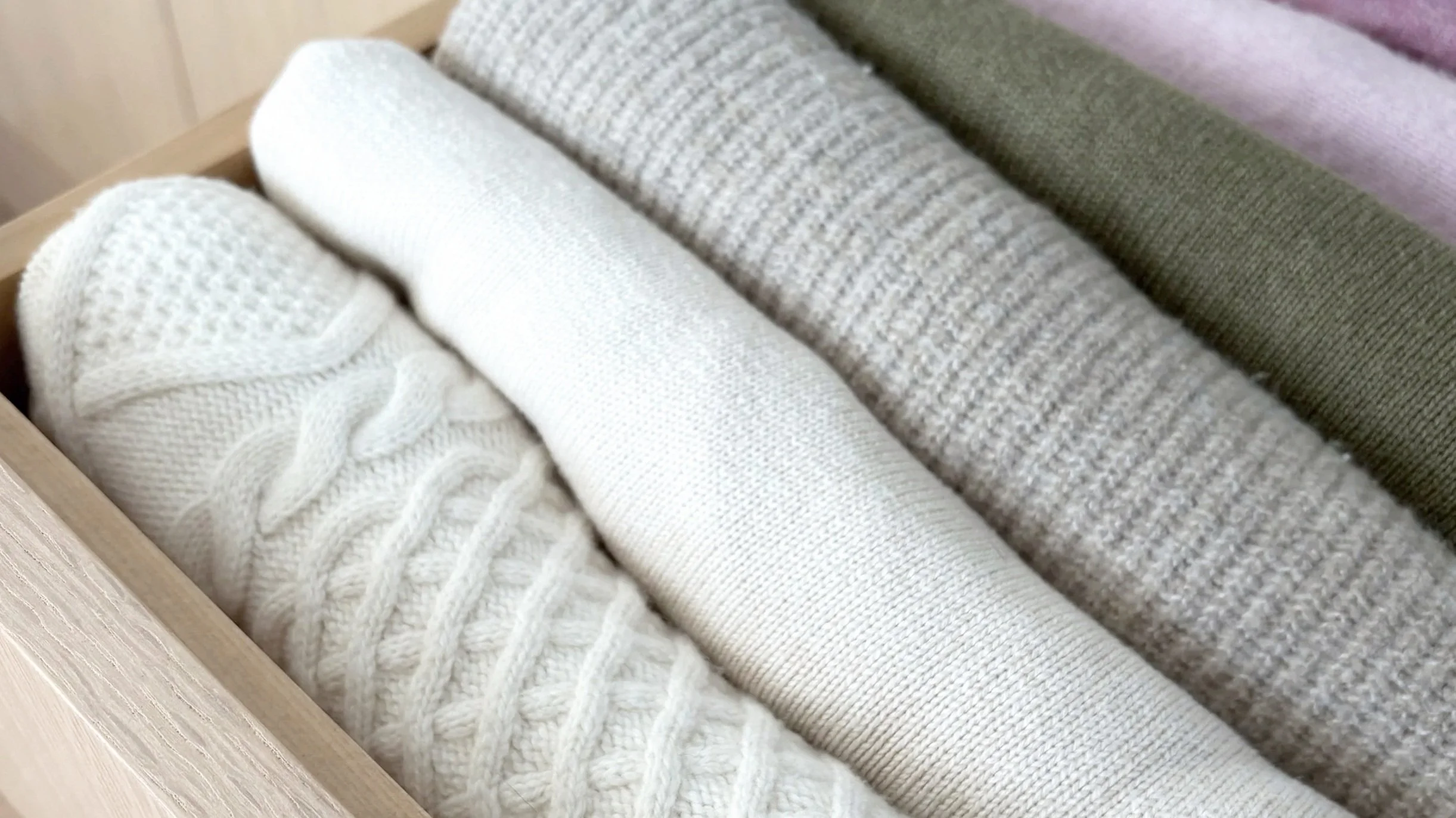 Six rolled-up fabric pieces in neutral and earth tone colors arranged in a wooden drawer.