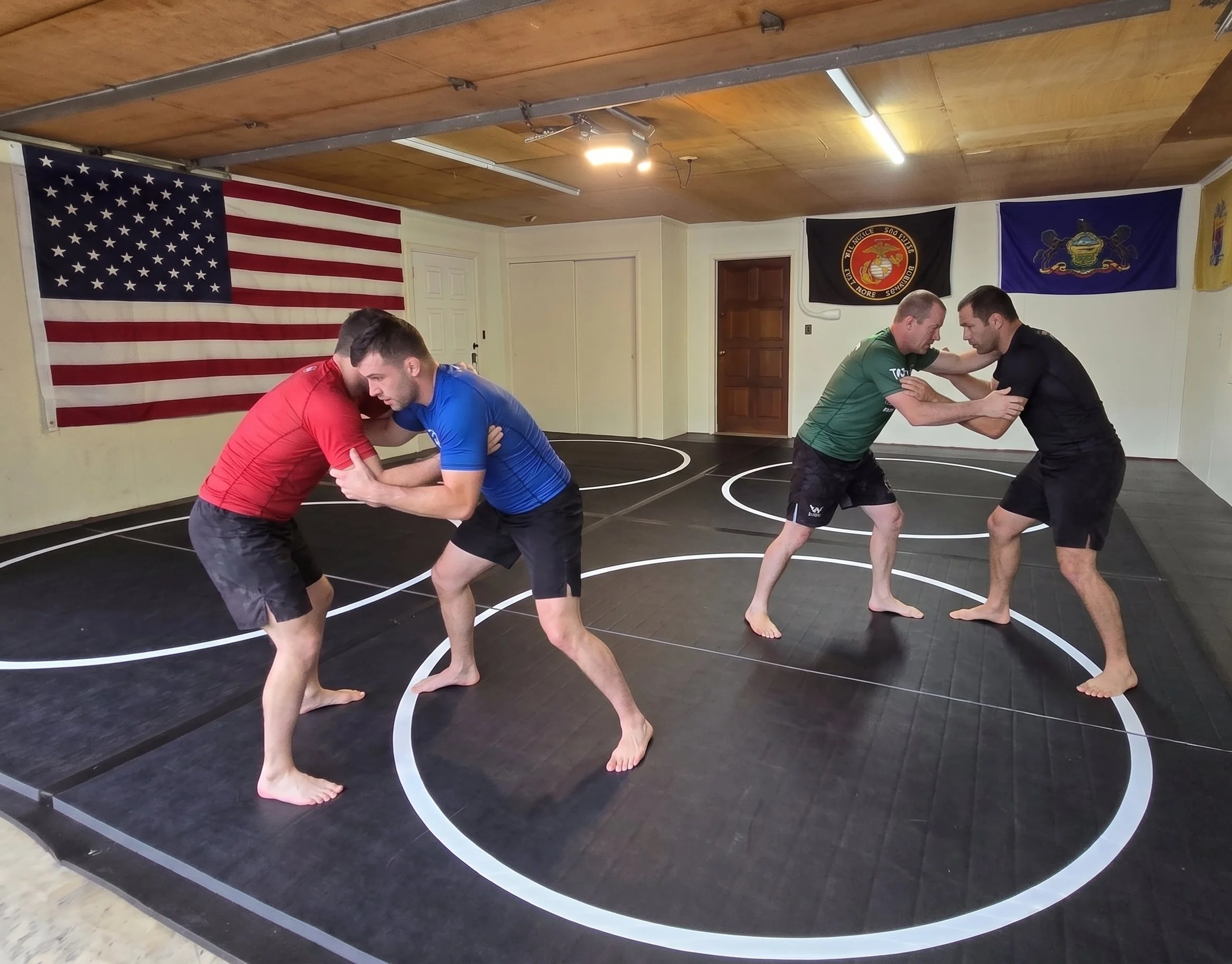 Men practicing Brazilian Jiu-Jitsu and wrestling grappling on black mats inside a sober living home training dojo in Pennsylvania