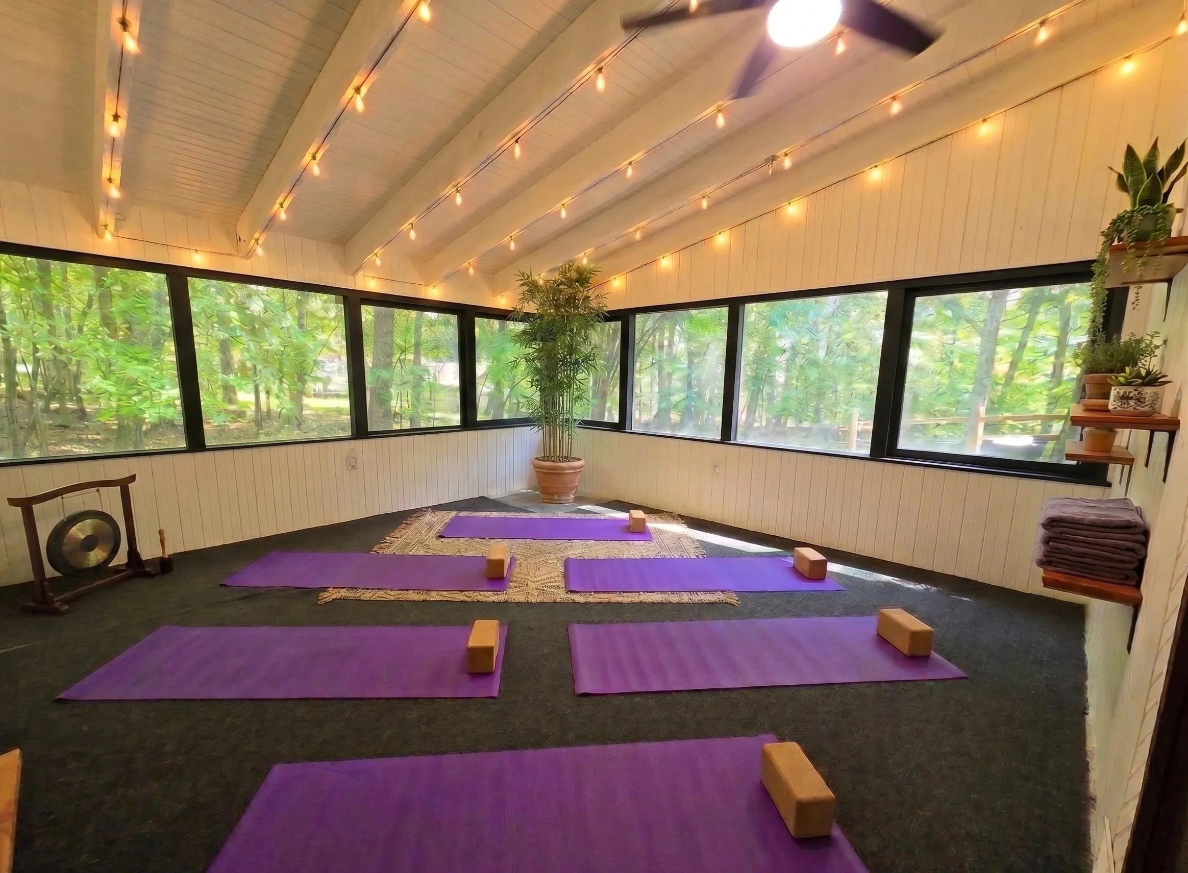 Peaceful yoga and meditation room with purple mats, string lighting, and panoramic forest views at New Soil Sober Living in Northeast Pennsylvania