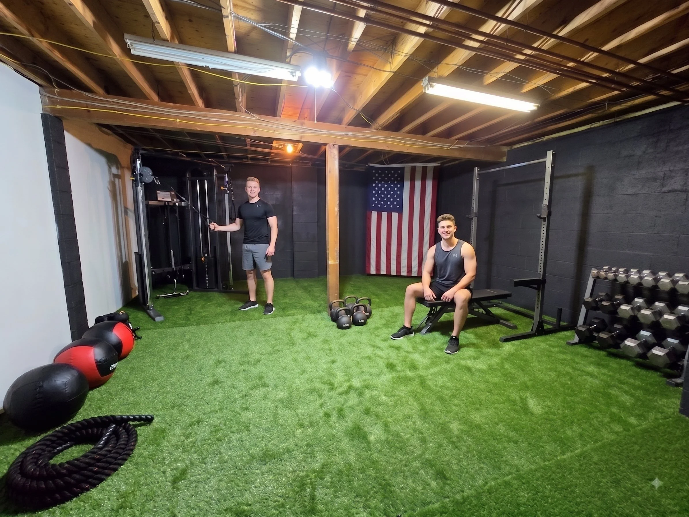 Two young men using a custom home gym with green turf flooring, free weights, cable machine, and an American flag at New Soil Sober Living in Northeast PA