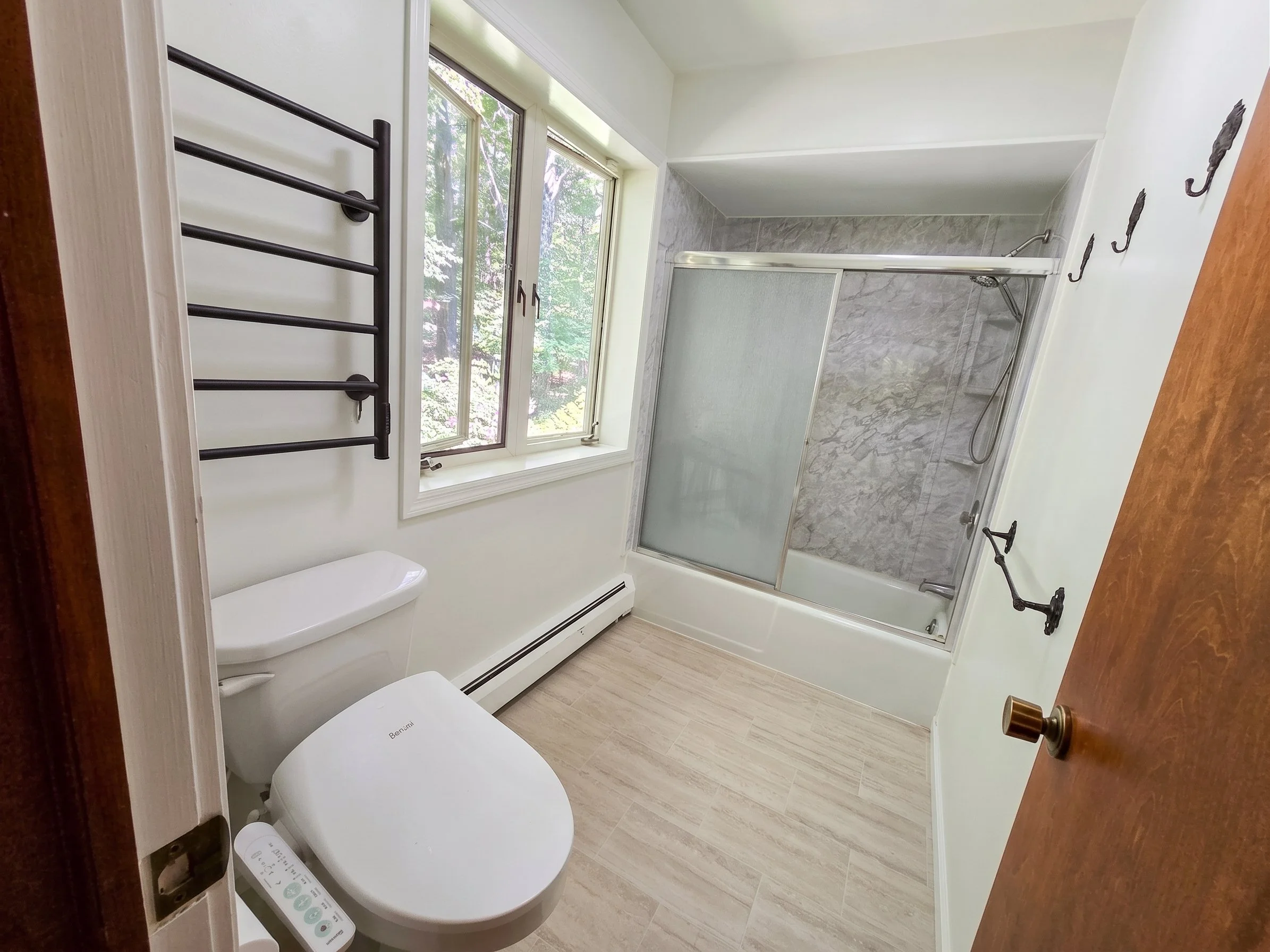 Bright, modern sober living bathroom with white walls, tiled floor, bidet toilet, towel rack, and glass sliding shower doors