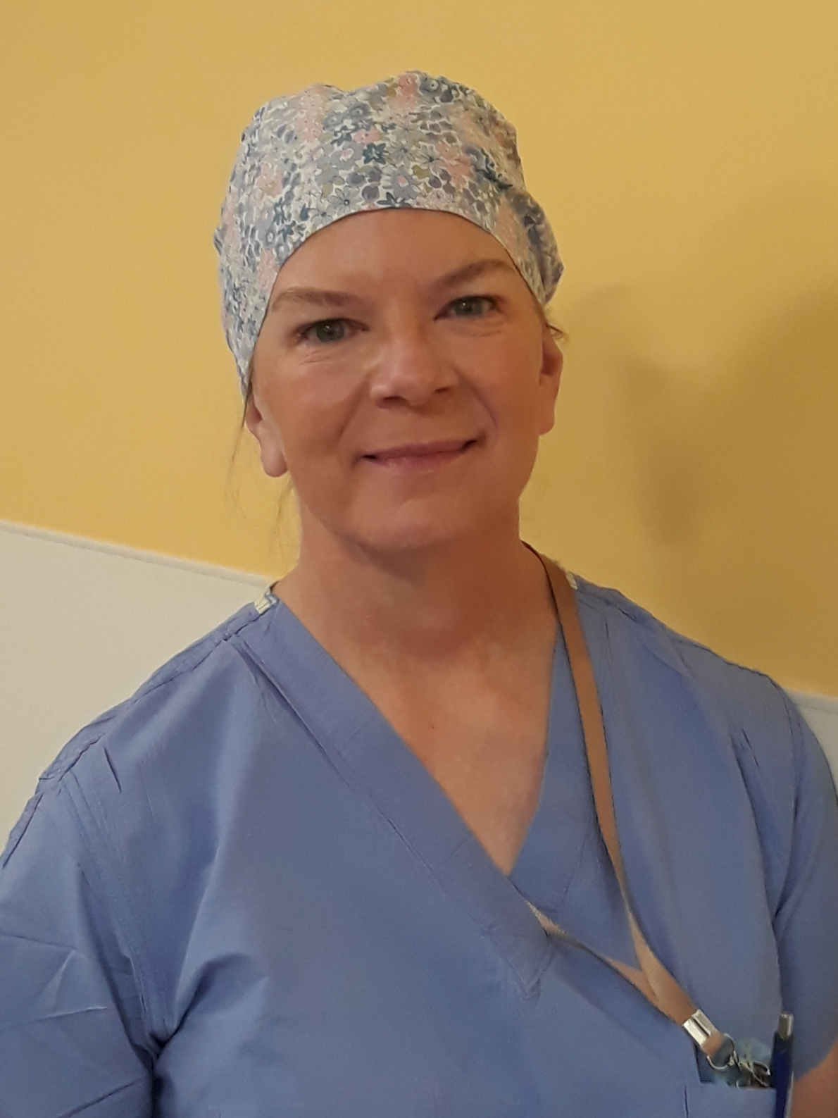 A healthcare professional in scrubs and a floral surgical cap smiling in a medical setting.
