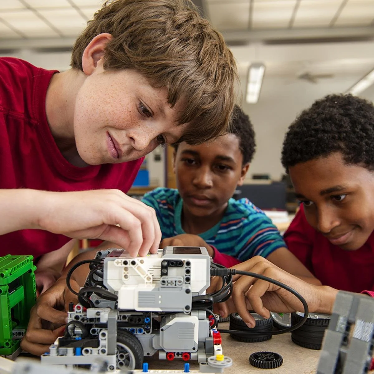 An instructor teaching two boys how to build a robot using a robotic kit in a classroom.