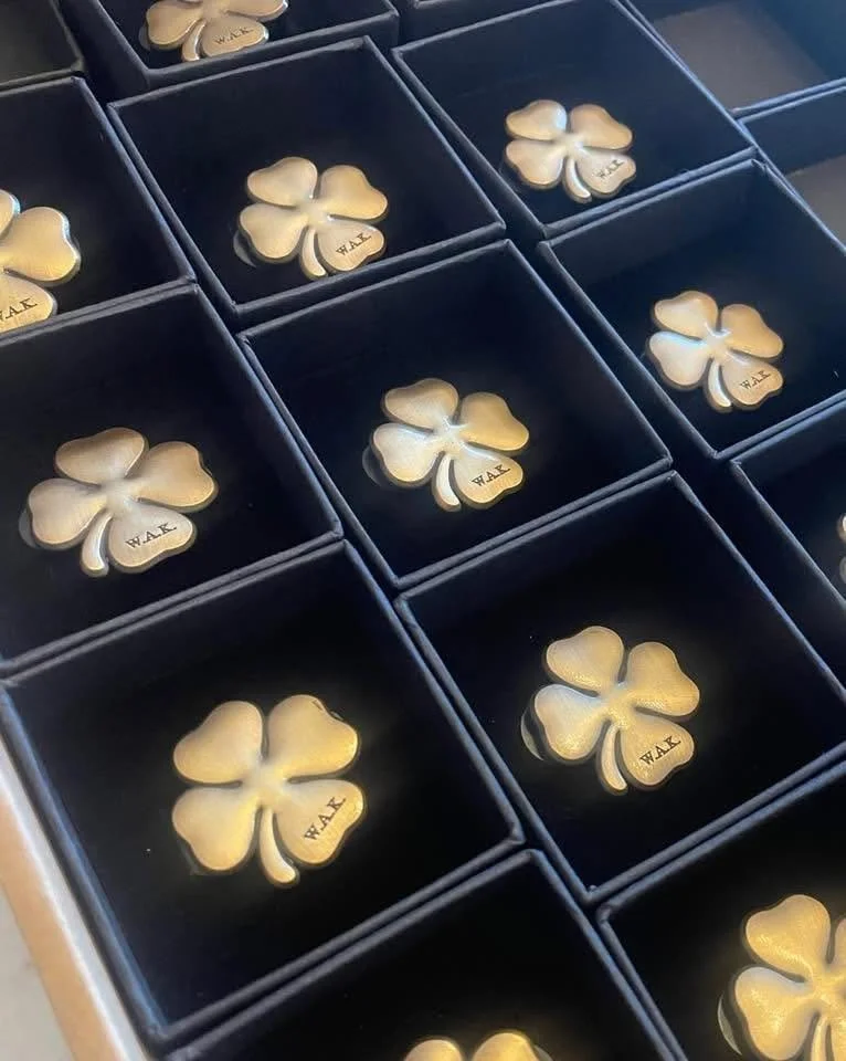 Gold shamrock pins with 'WAL' engraving in a black display box with individual compartments.