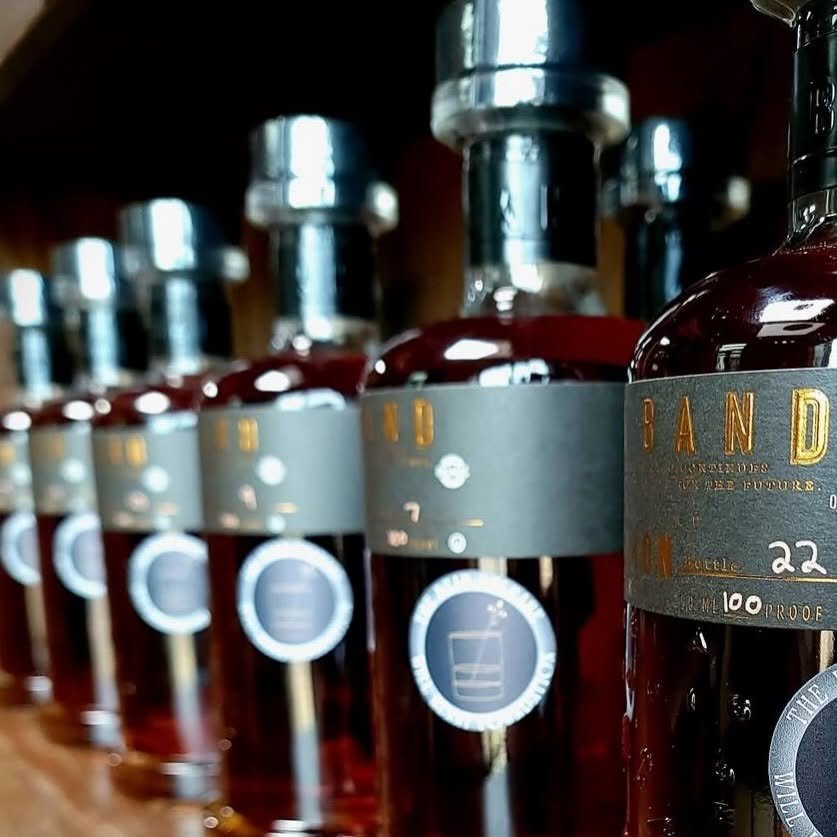 Multiple bottles of John Sandler whiskey on a wooden shelf, with focus on the front bottle.