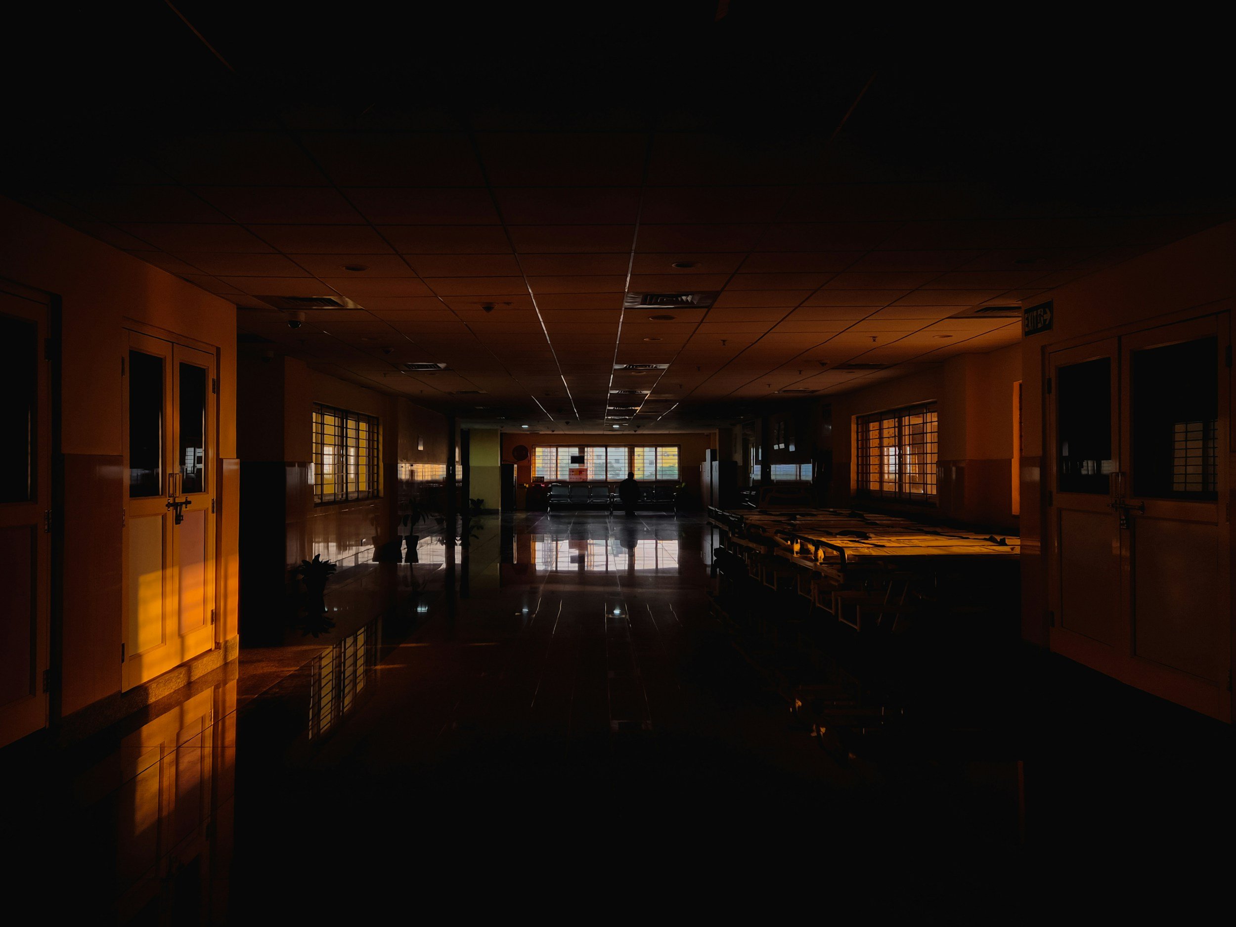 Dimly lit indoor corridor with chairs and windows at the end, warm sunlight streaming through.