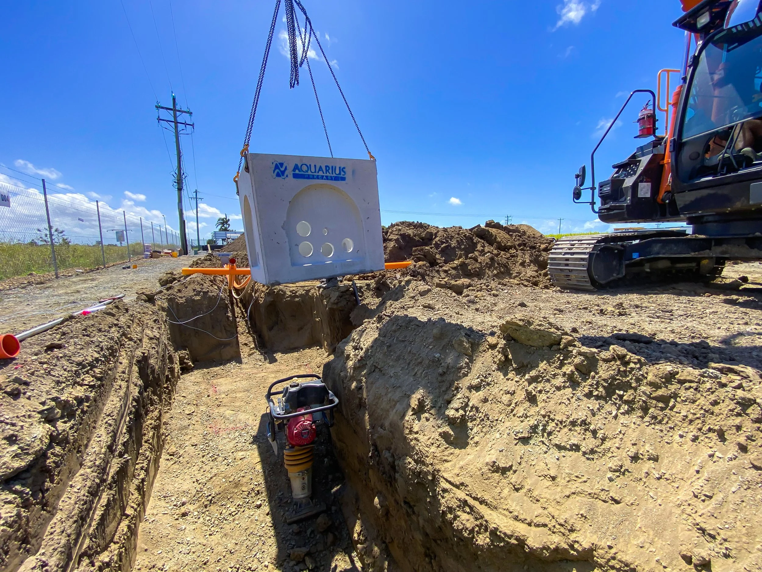 Construction site with a large excavation trench, construction equipment, trenches, and equipment including a small excavator and machinery, under a clear blue sky.