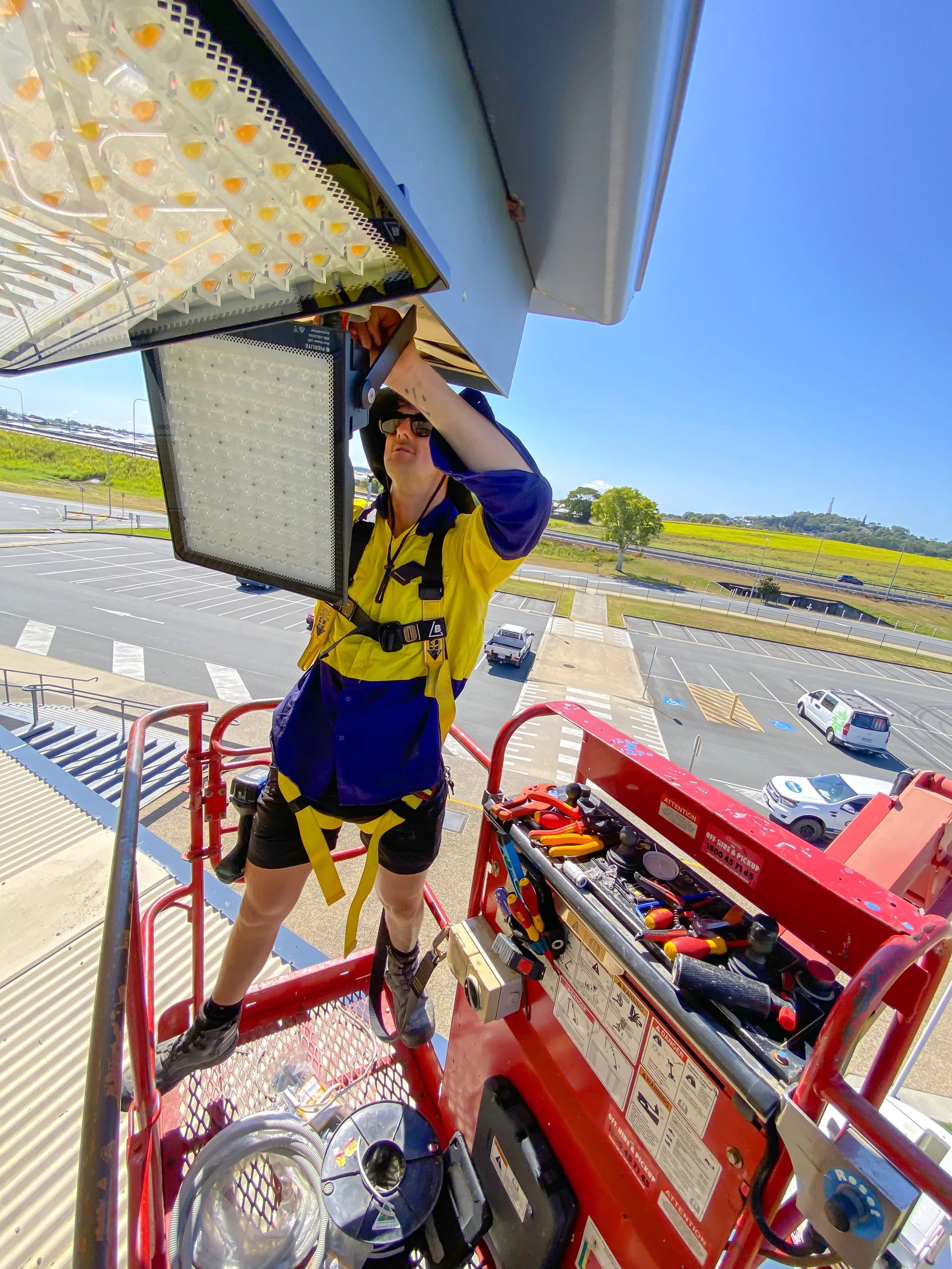 A person working on a utility lift with tools and equipment around them, outdoors on a sunny day.