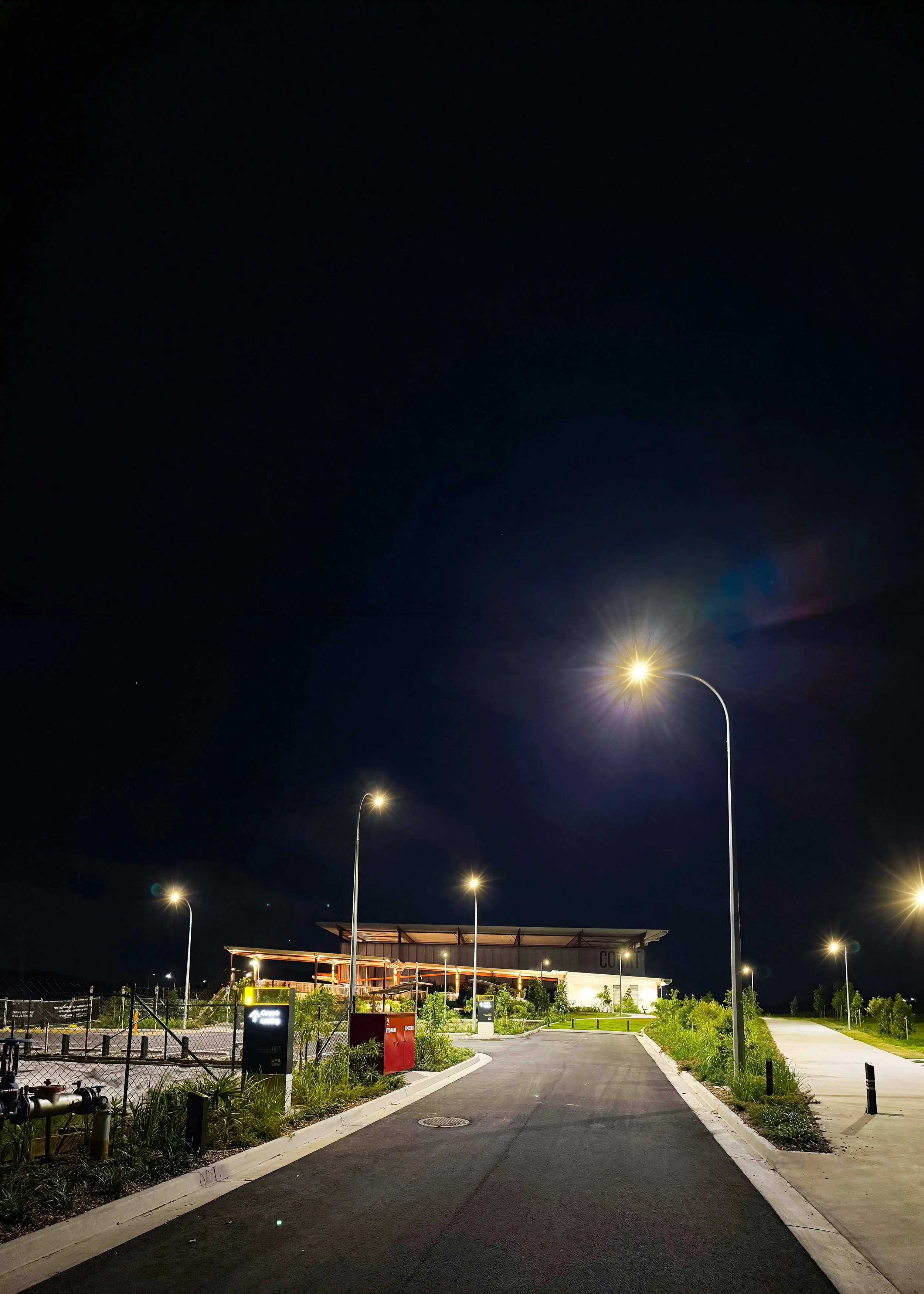 Night view of a parking lot with illuminated streetlights, a covered seating area, and surrounding greenery.