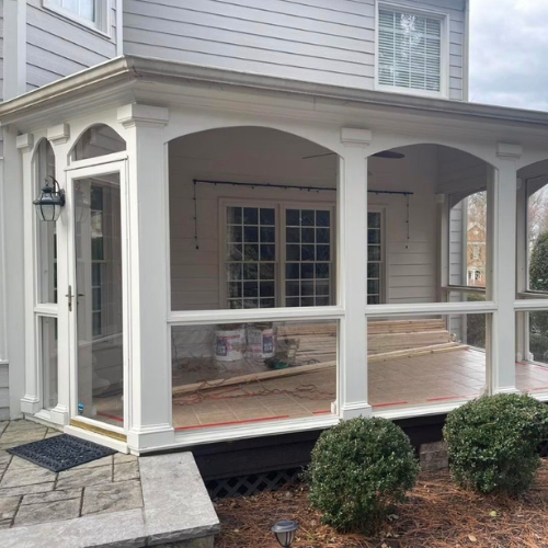 A screened porch under construction attached to a house, with some tools and materials visible inside.