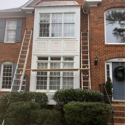 Scaffolding in front of a townhouse undergoing window installation or repairs, with two ladders on either side and bushes at the base.