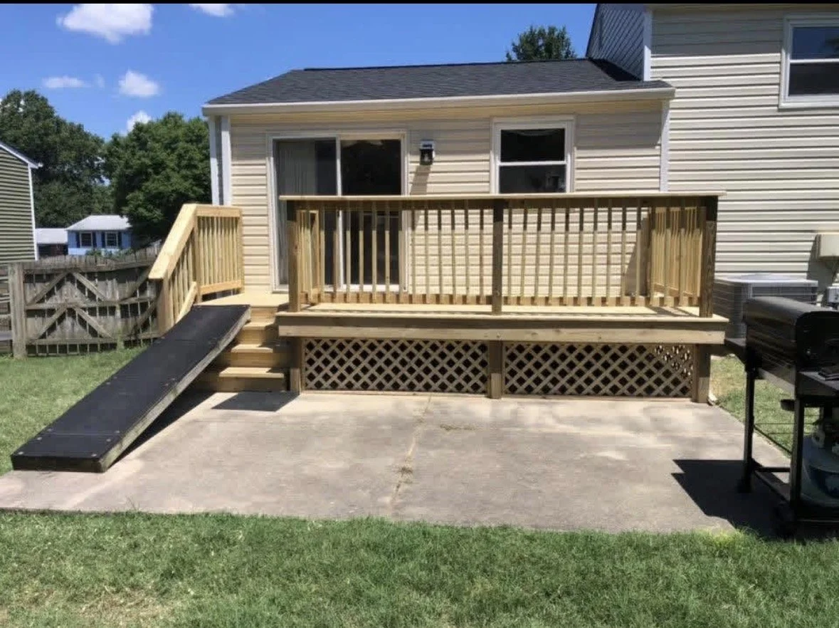 new wooden deck with stairs, sliding glass door, and ramp attached to the back of a house, with a barbecue grill on the patio