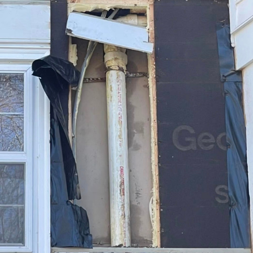 Construction site revealing exterior wall with window, insulation, piping, and wooden framing.