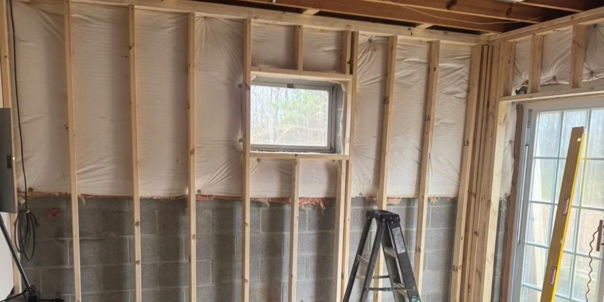 Interior wall under construction with exposed wood framing, insulation, a small window, and a stepladder.