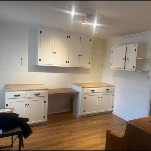 Empty kitchen with white cabinets, wooden countertops, and hardwood floor.