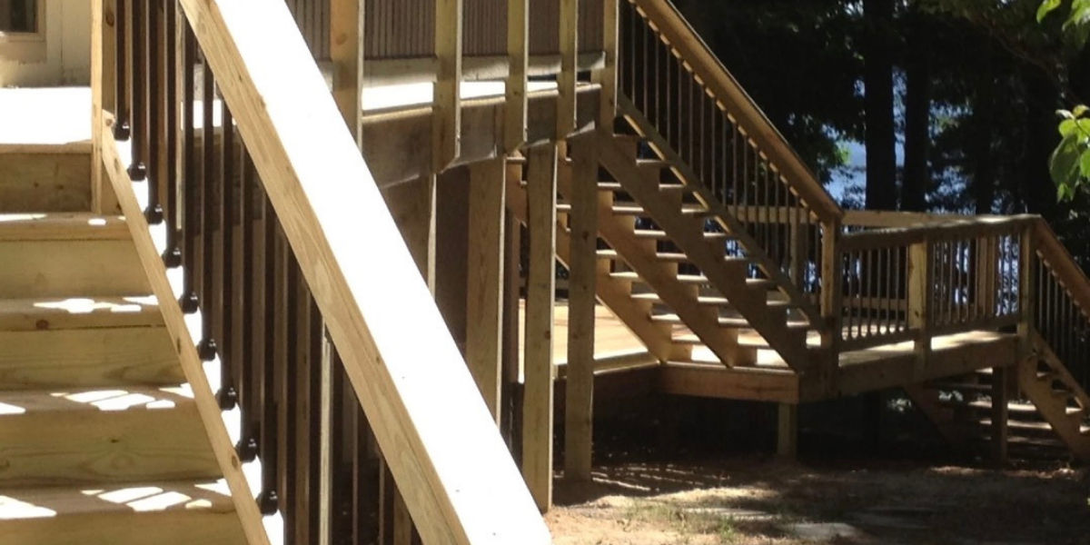 Newly built wooden deck and staircase in a backyard, with trees in the background.