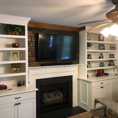 Living room with white built-in shelves on either side of a fireplace, a large flat-screen TV above the fireplace, and various decorative items and framed photos on the shelves.