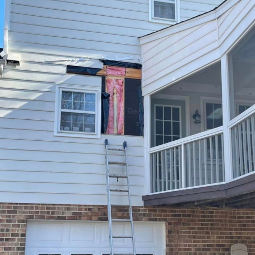 A ladder leaning against a house under construction or repair, with exposed insulation and framing around a window.