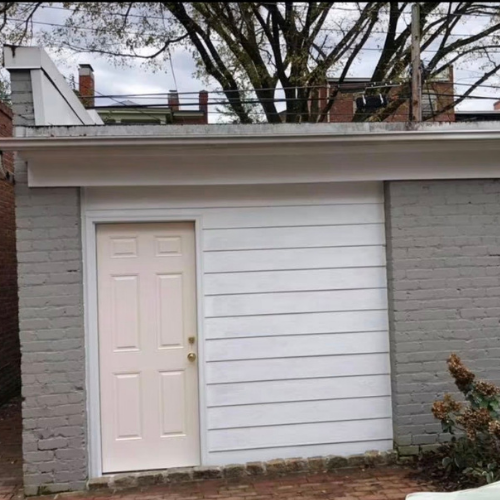 A small, white wooden door set into a gray brick wall outside a building.
