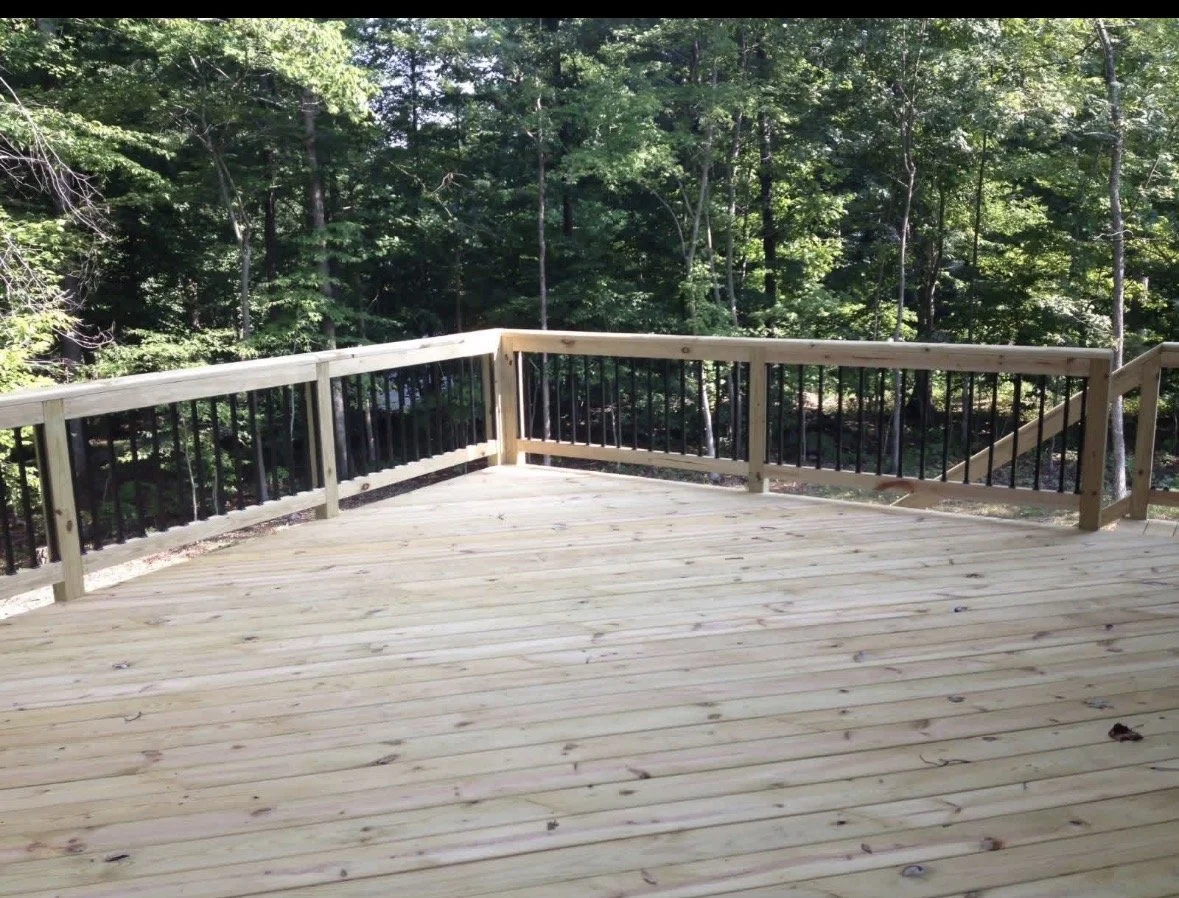 Wooden deck with black railing overlooking a lush green forest.