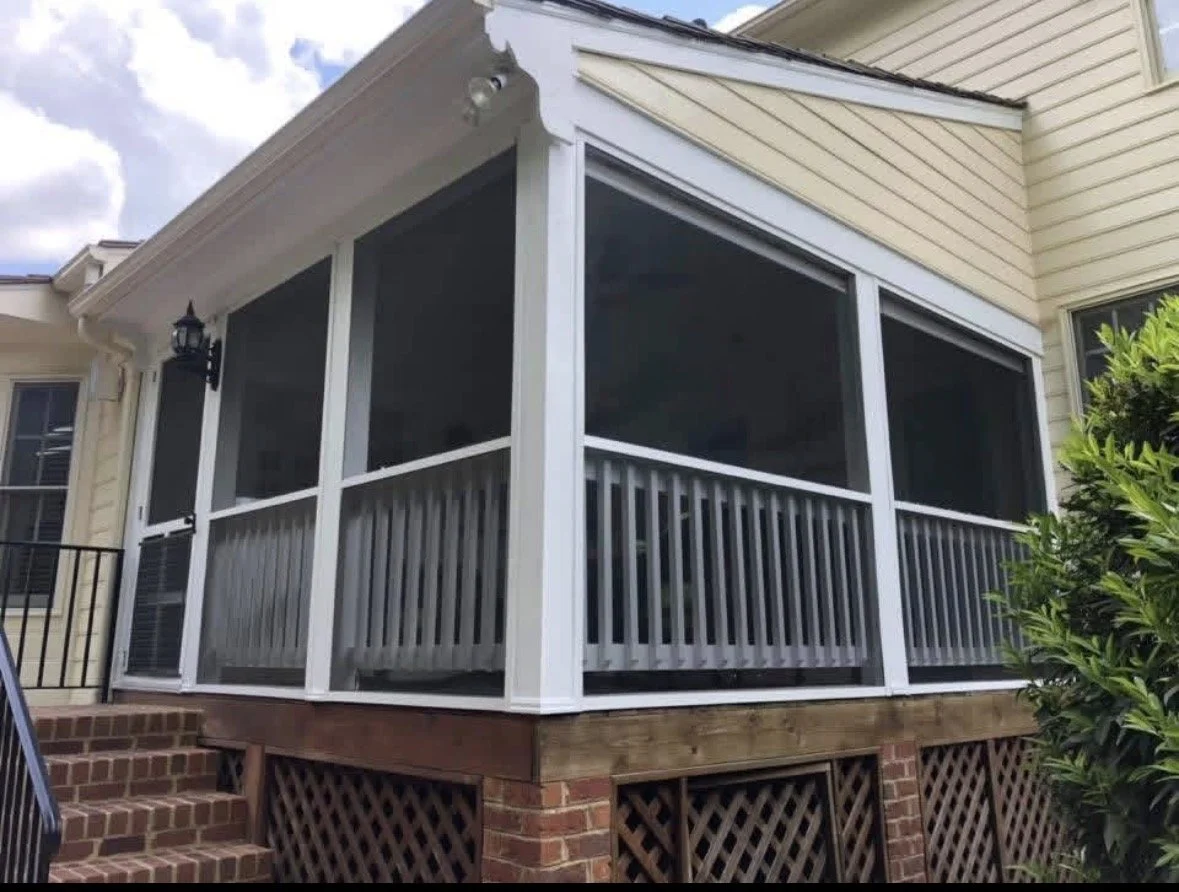 A screened-in porch or patio area on a house, with white framing and a lattice skirt below. The porch is elevated with brick steps leading up to it.