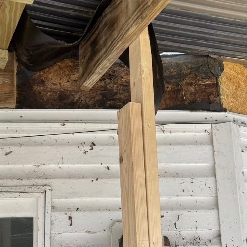 Close-up of a wooden post attached to the exterior wall of a building, with some construction materials and debris nearby.