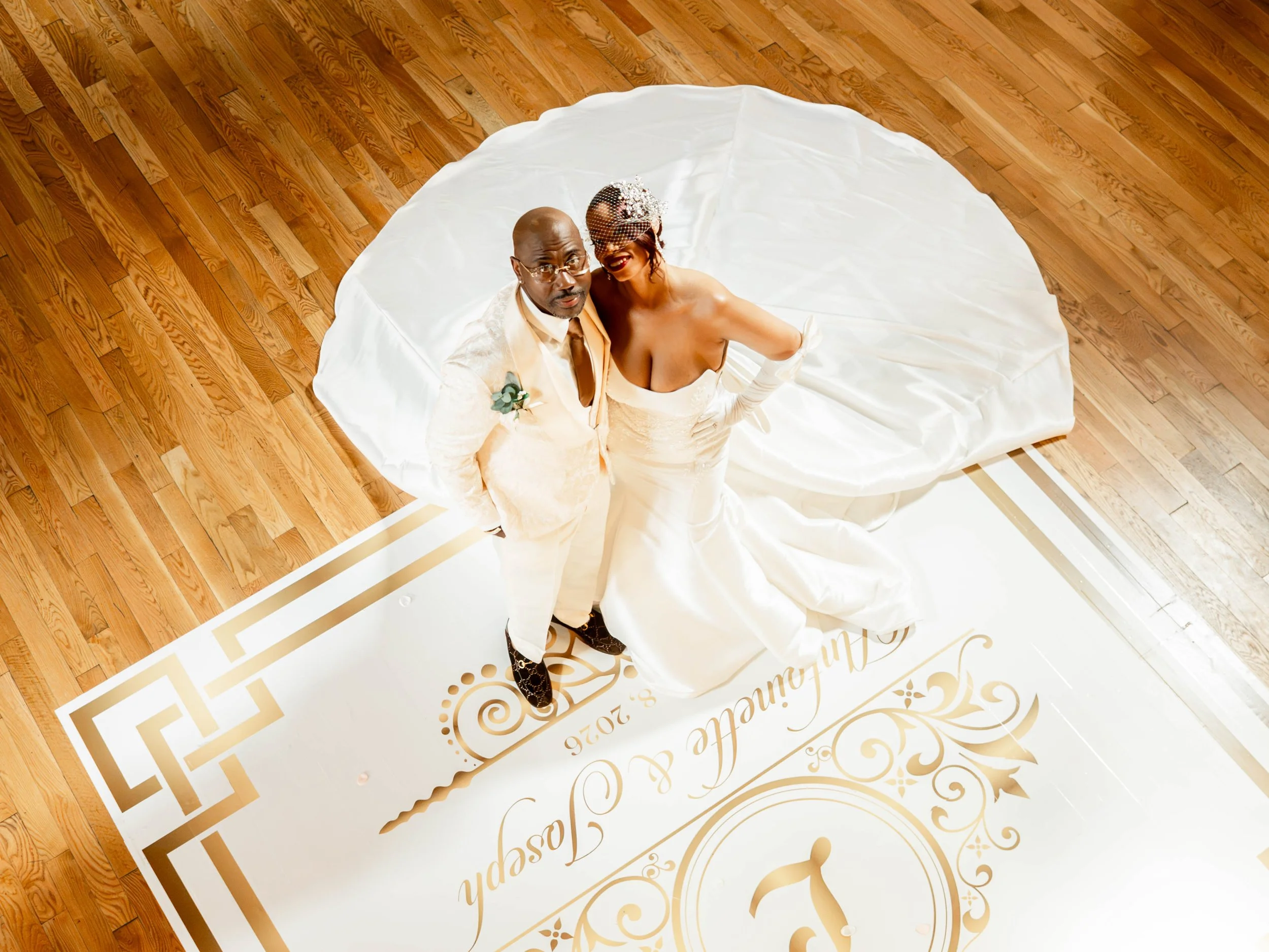 A bride and groom looking up at the camera as they stand on a wedding dance floor.