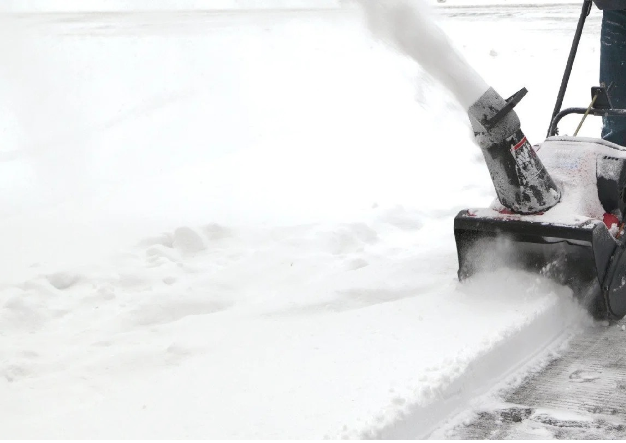 A person using a snowblower to clear snow from a sidewalk or driveway in a snowy outdoor setting.