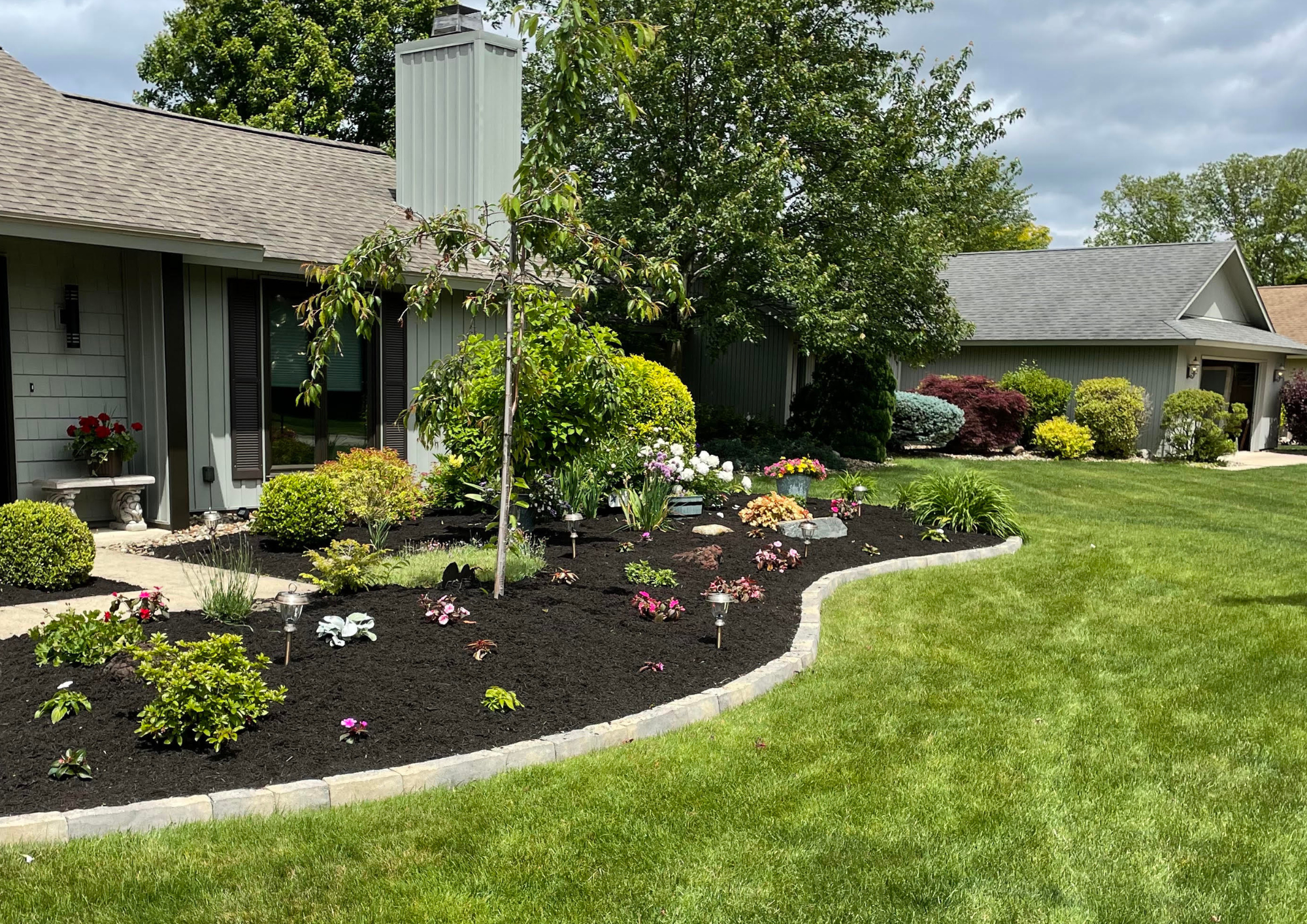 A well-maintained front yard with a flower bed and trees in a suburban neighborhood.