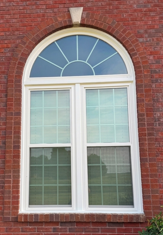 White arched window installed in a red brick exterior