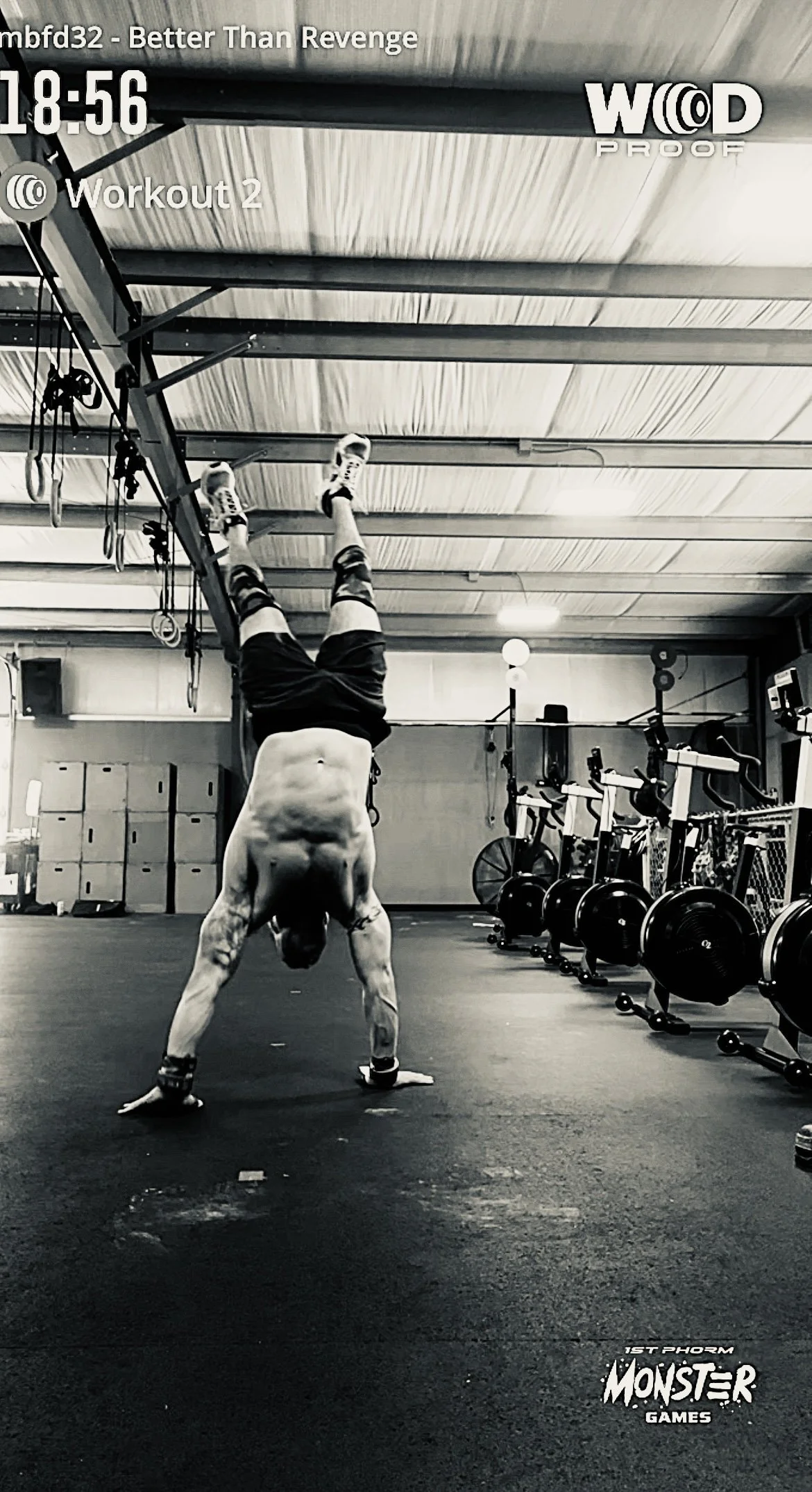A man is performing a handstand in a gym, with gym equipment such as rowing machines and weights visible in the background.
