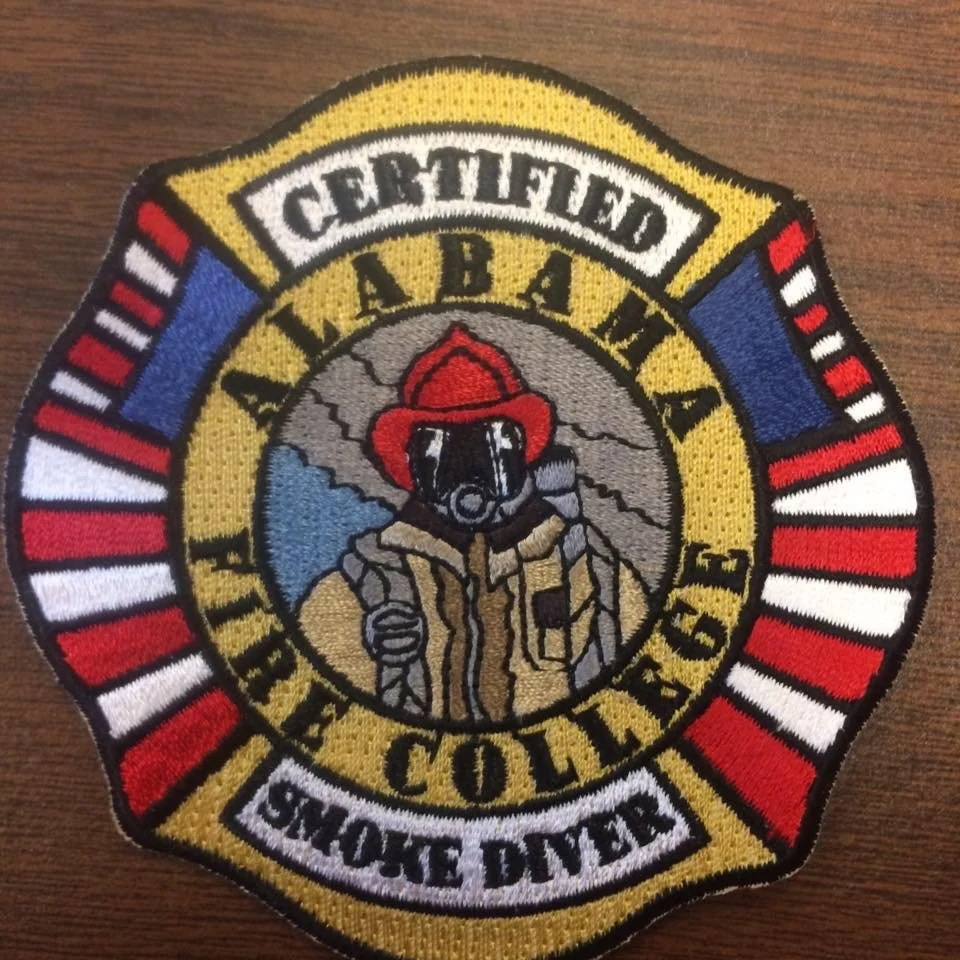 Colorful embroidered patch for Alamaba Fire and Rescue, featuring a firefighter in gear and a red helmet, with a mountain and lightning background.