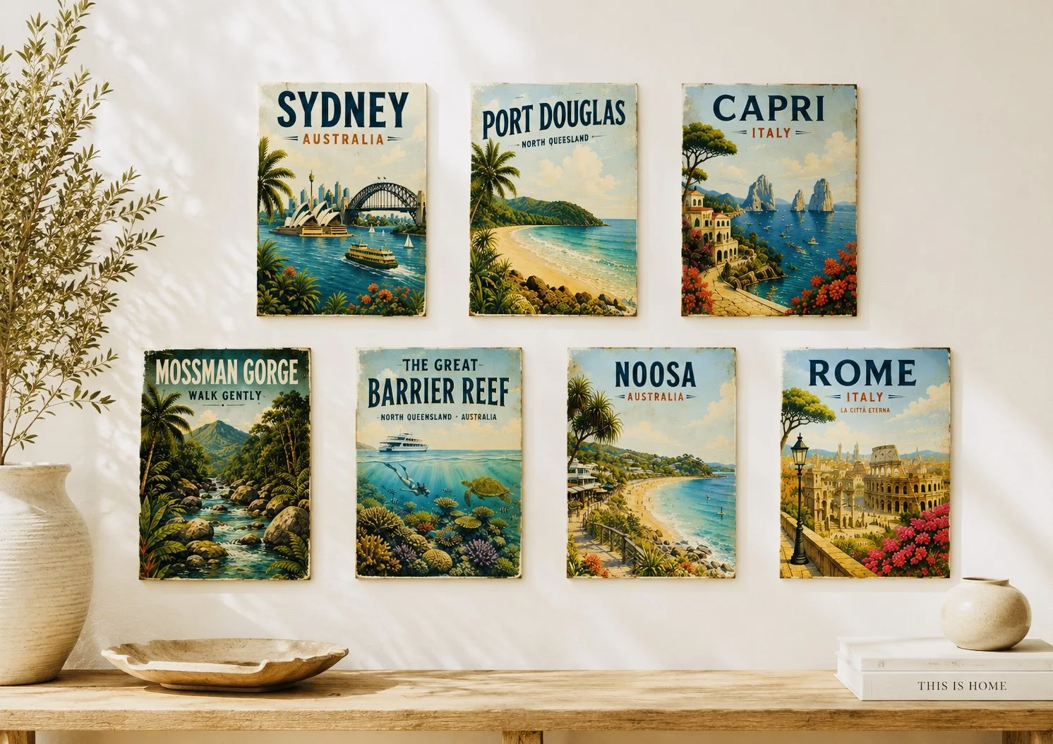 Decorative travel posters on a white wall, featuring destinations like Sydney, Port Douglas, Capri, Mossman Gorge, Barrier Reef, Noosa, and Rome with colorful illustrations of landscapes and landmarks.