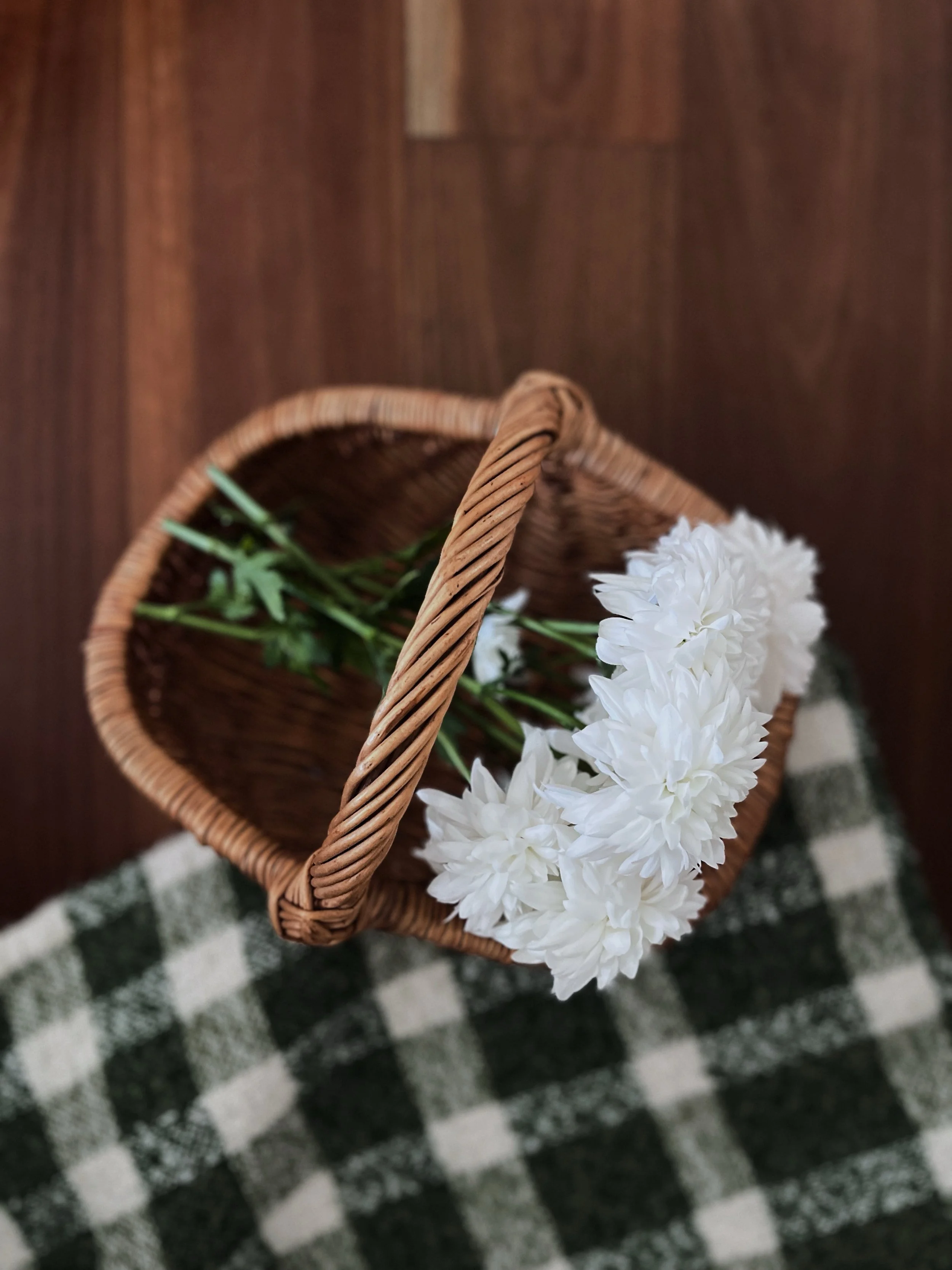 A wicker basket with white flowers and green foliage on a black and white checkered rug.