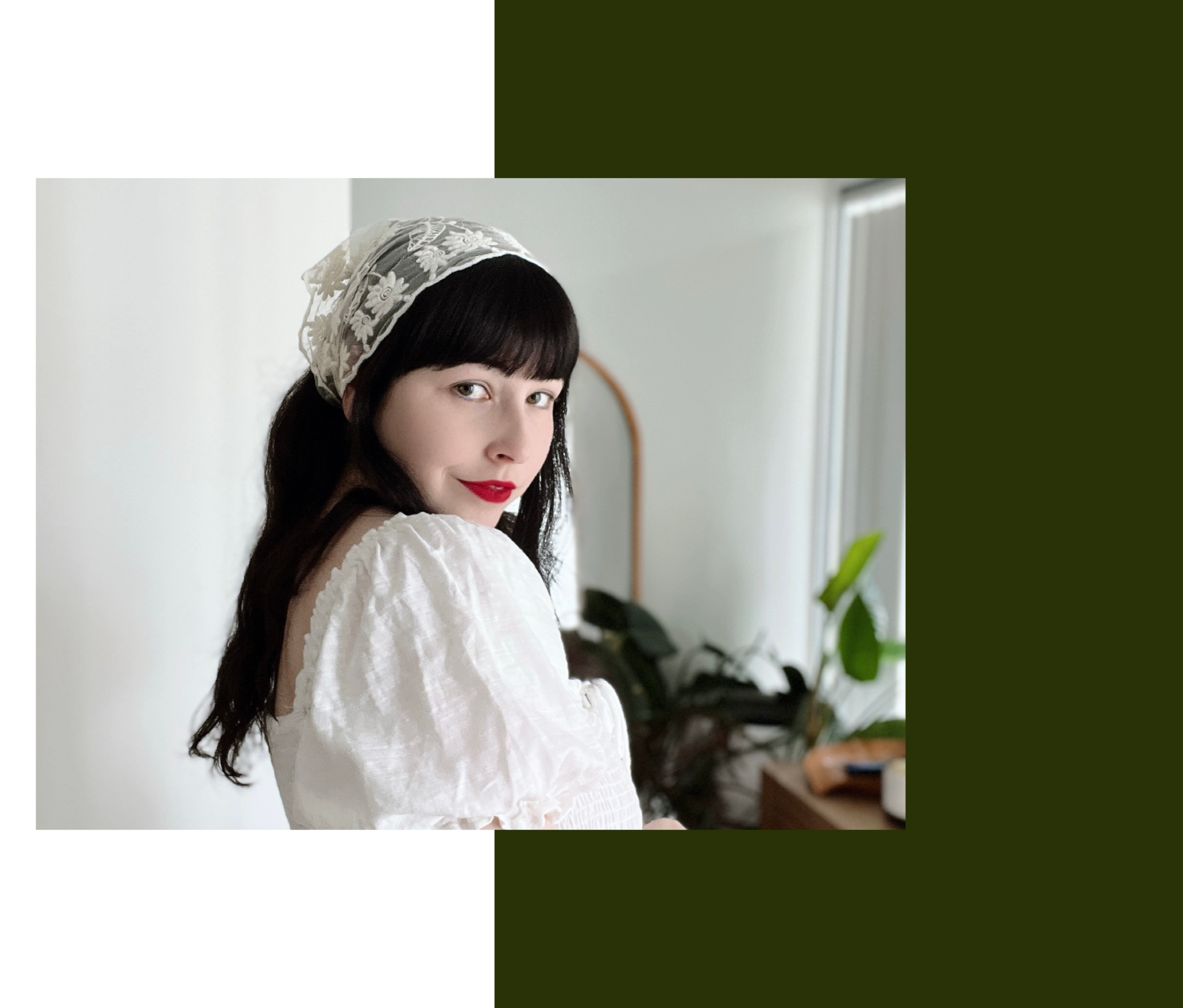 A woman with dark hair, dressed in a vintage-style white dress and lace headscarves, standing indoors with a neutral expression.
