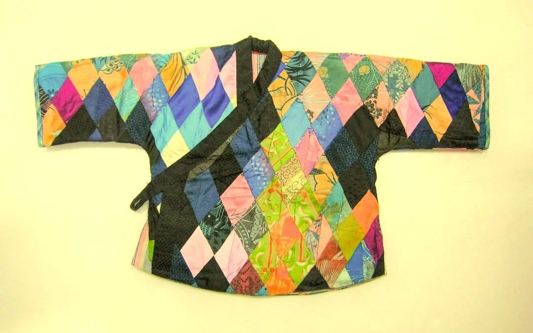 Colorful quilted kimono-style garment with diamond patchwork pattern spread out on a light-colored surface.