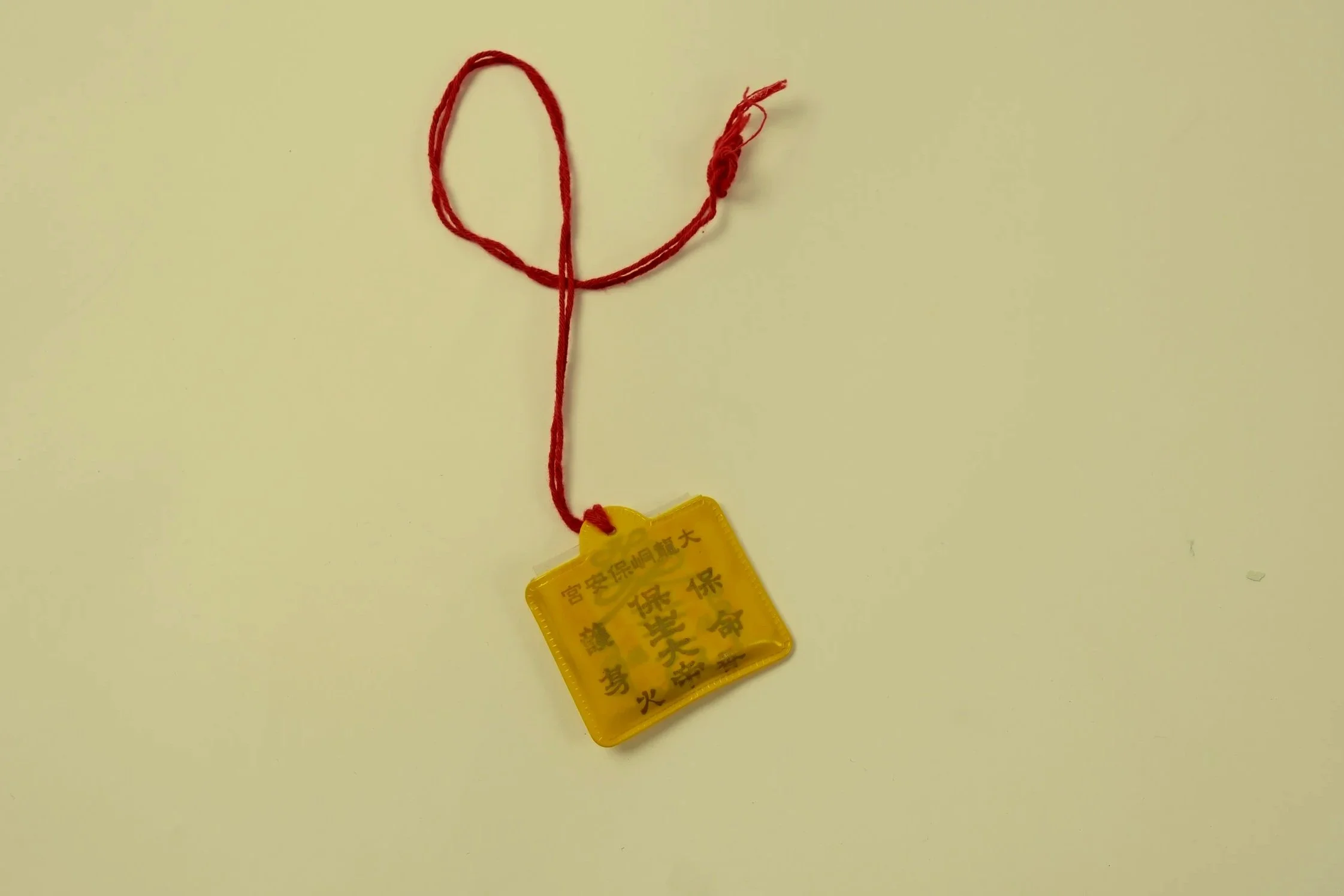 A yellow identification tag with Chinese characters attached to red string. The string is shaped like a heart and is tied to form a loop.