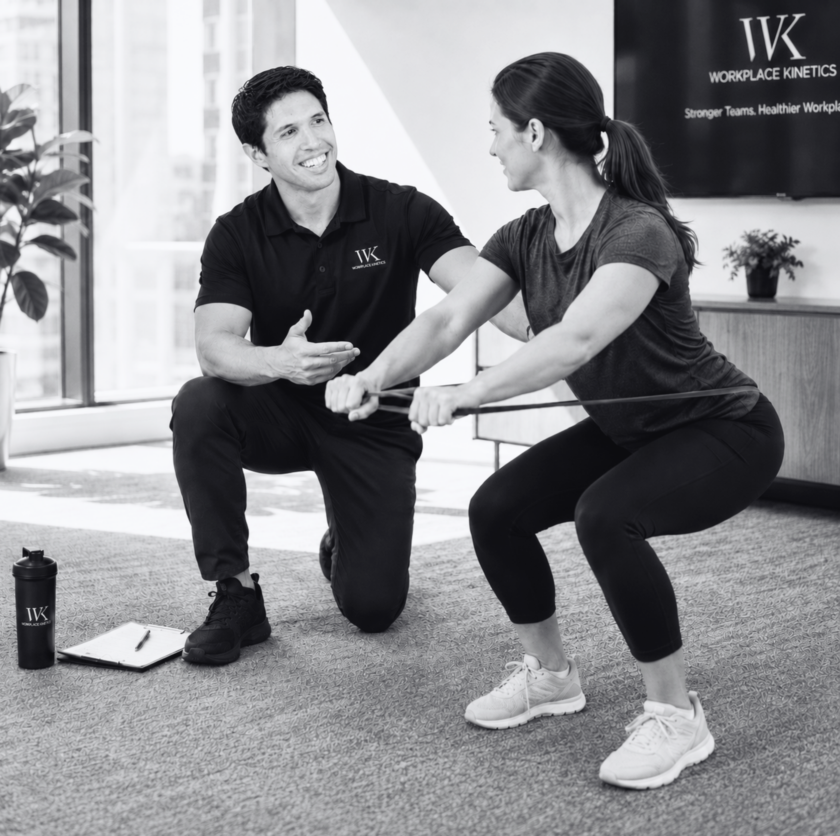 A fitness trainer assisting a woman with resistance band exercises in a gym, with a black water bottle, clipboard, and pen nearby.