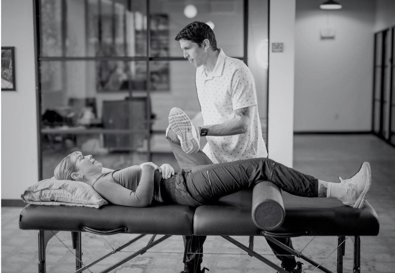 A physical therapist assisting a woman with leg exercises on a treatment table in a modern clinic.