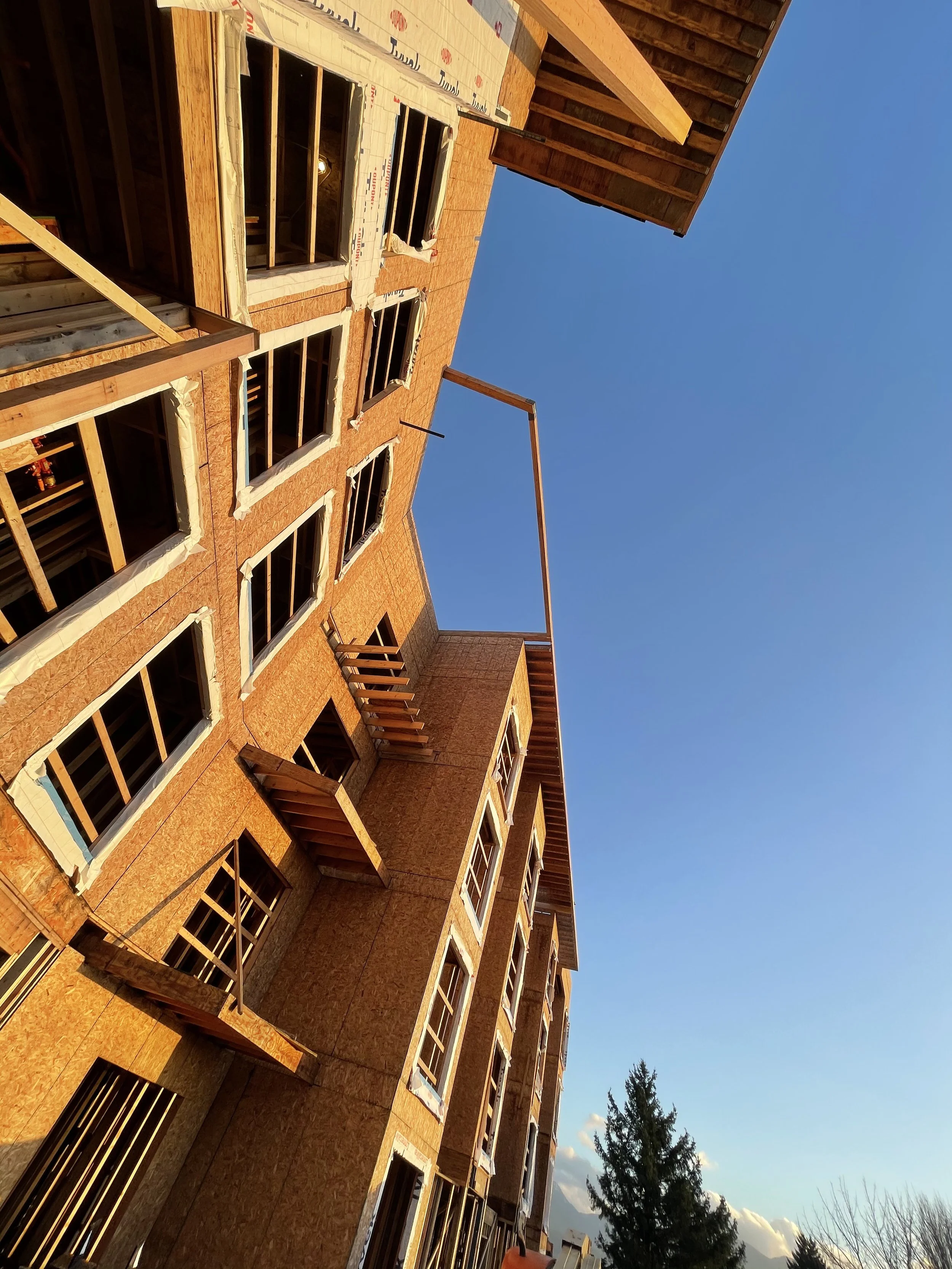 A multi-story brick building under construction with window openings and scaffolding, with trees and blue sky in the background during daylight.