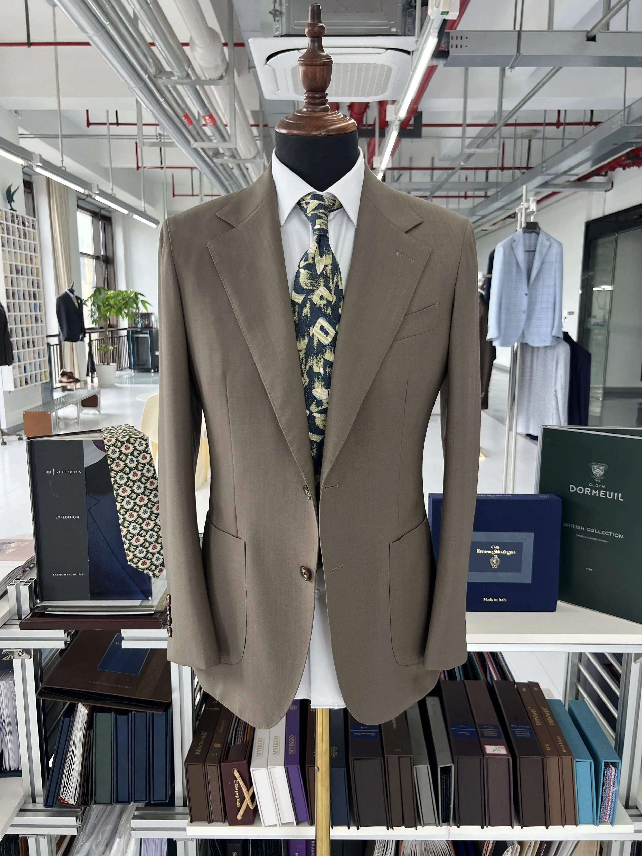 A beige suit jacket with a white shirt and a patterned tie on a mannequin in a store. In the background, there are shelves with various books and boxes.