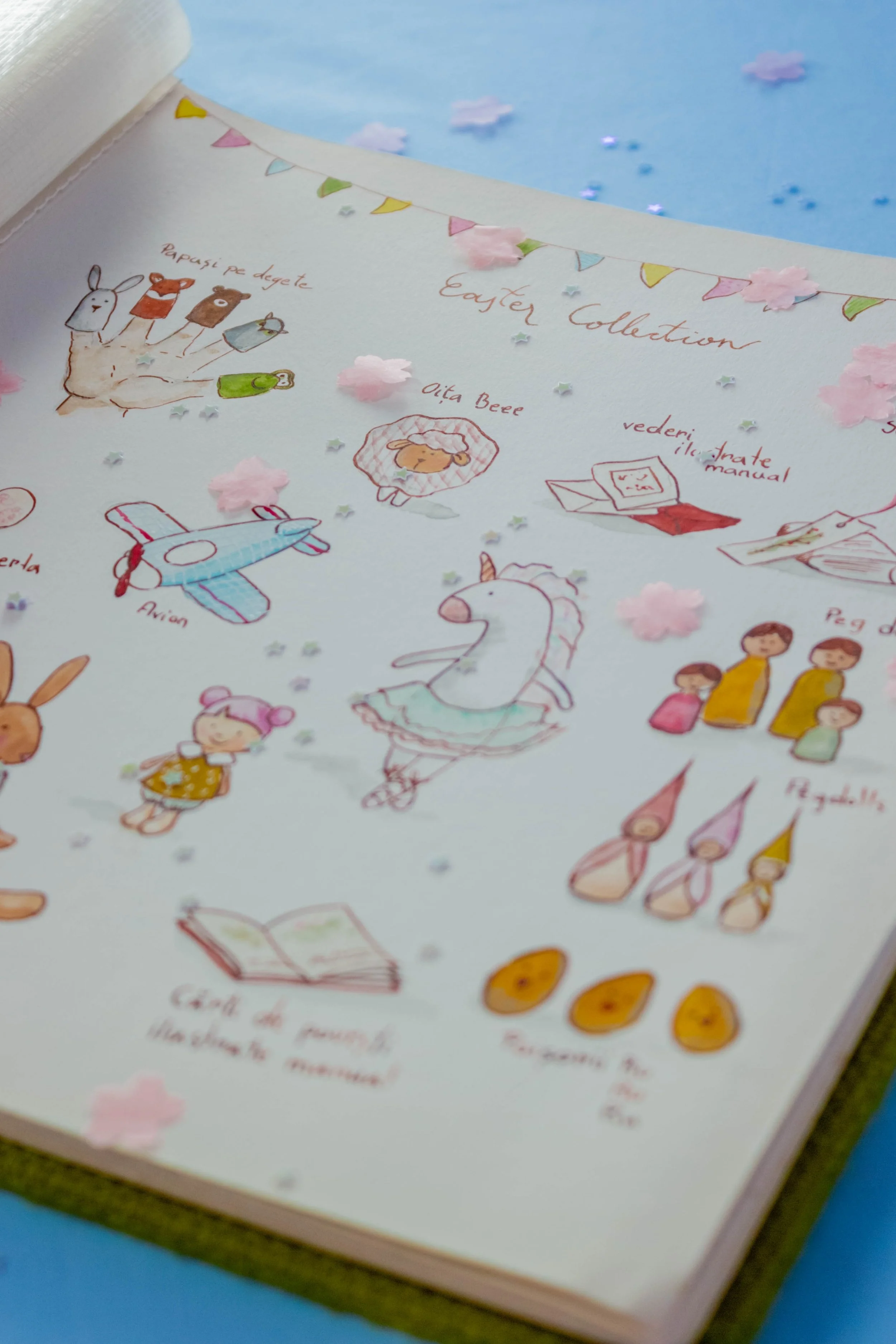 Page from an illustrated Easter collection with drawings of animals, a unicorn, and children, decorated with pink cherry blossom paper flowers and small star confetti, featuring notes about Easter activities and crafts.