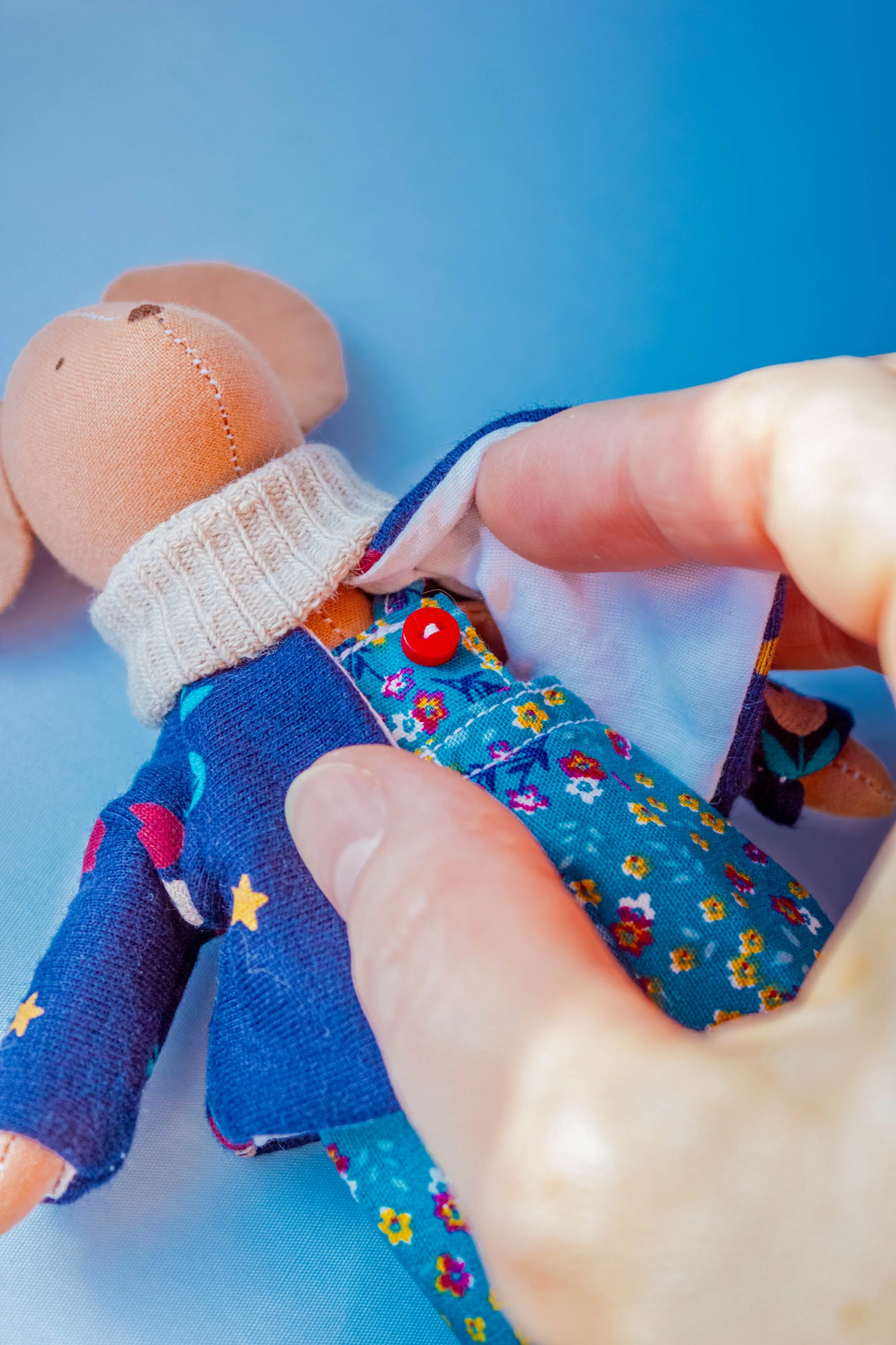 Close-up of human hand holding a small, fabric doll dressed in colorful clothing against a blue background.