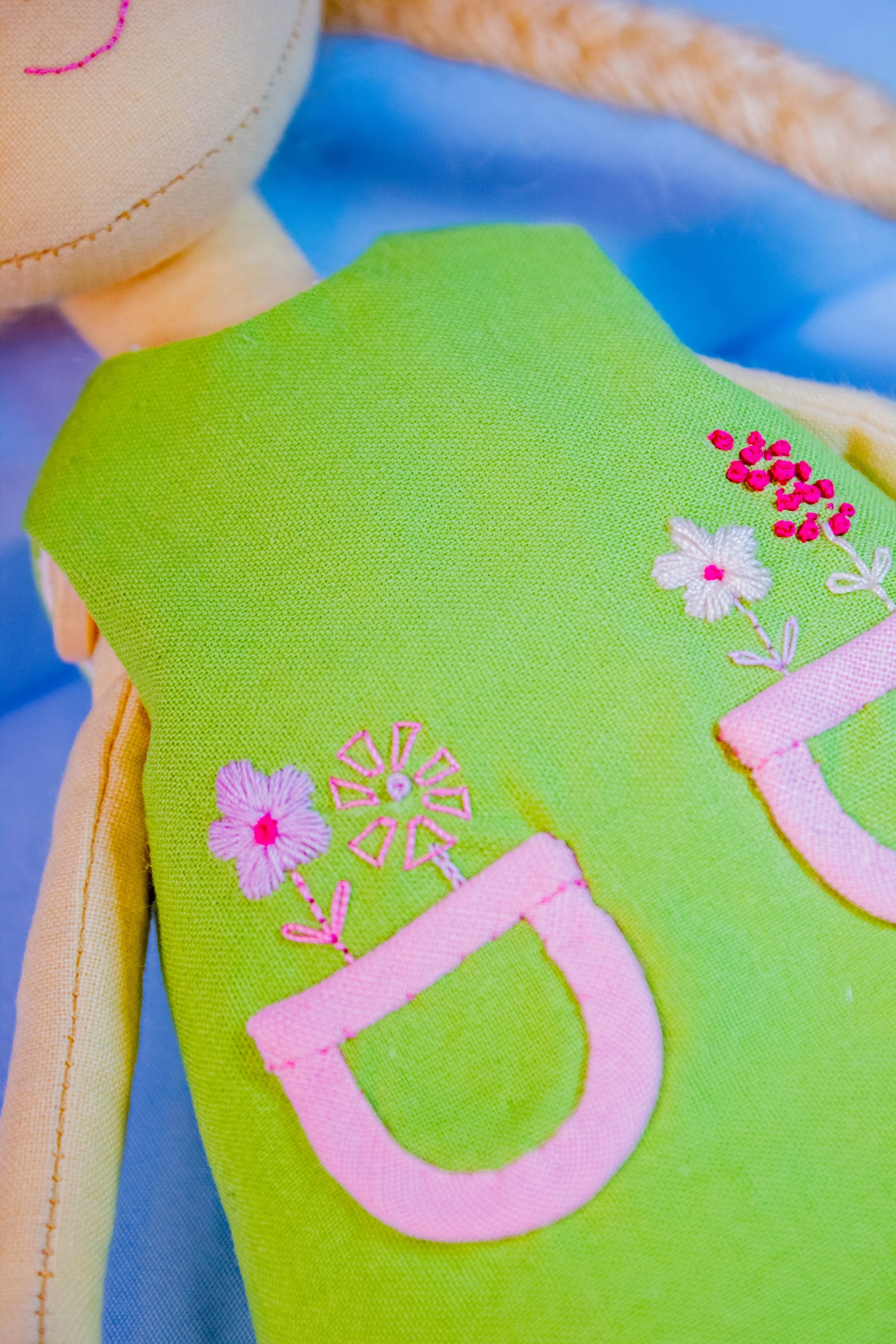 Close-up of colorful embroidered fabric featuring pink and white flowers, a pink letter 'U', and green background.